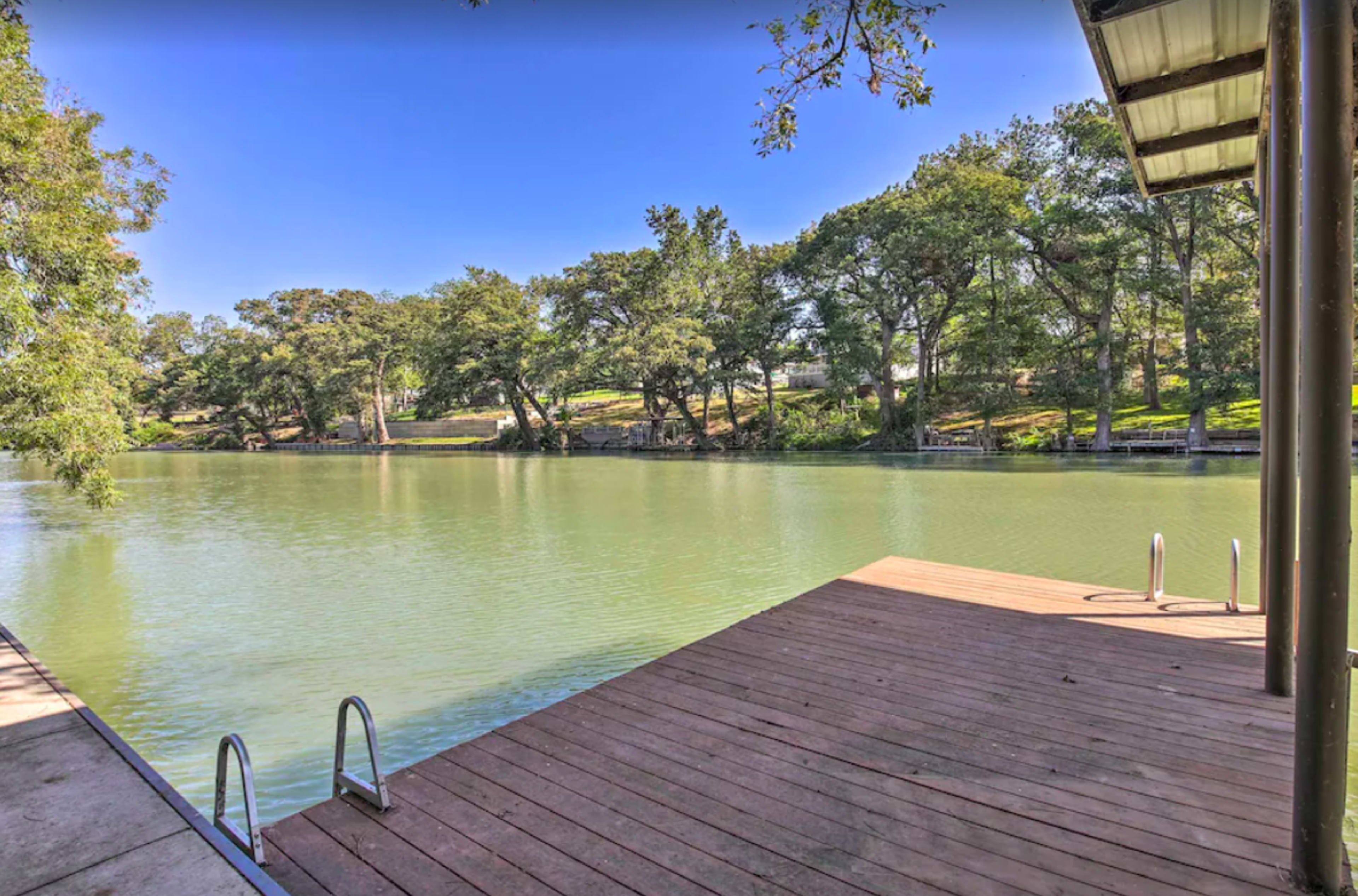 A wooden platform extends over a calm green river surrounded by lush trees on both banks.