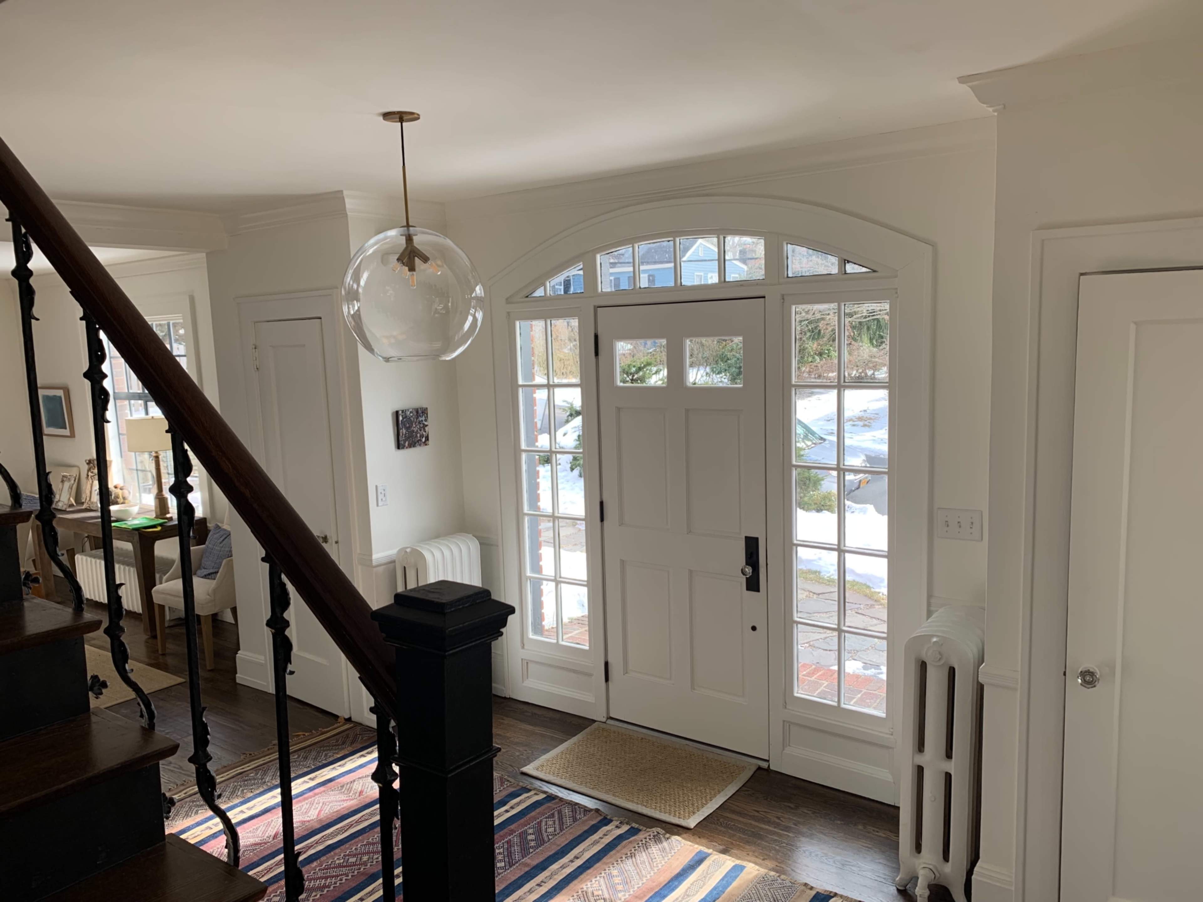 The entryway features a staircase to the left, a round pendant light, and large windows allowing light to fill the space.