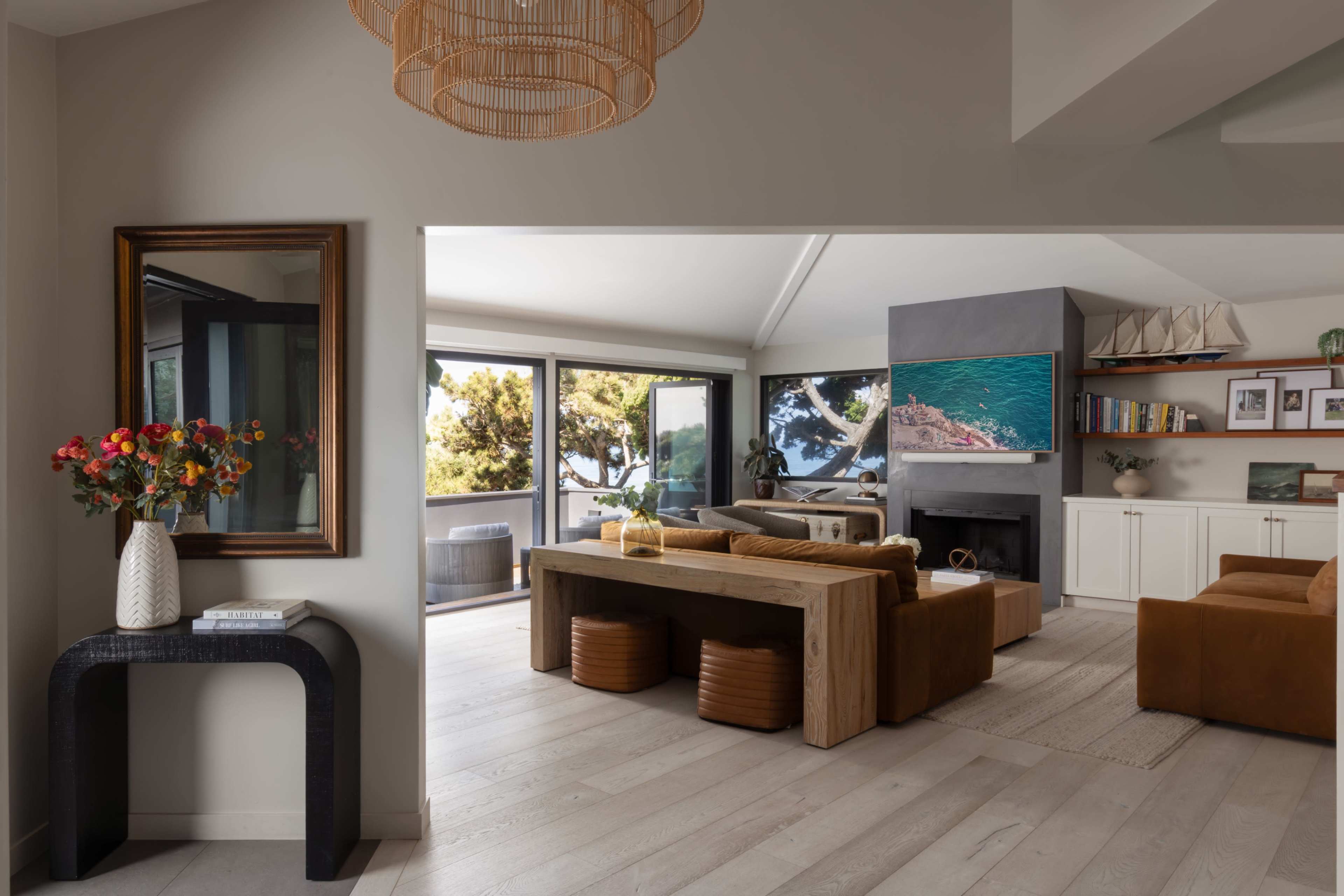 The image shows a modern, open-concept living space with a wooden dining table, a comfortable seating area, and large windows offering a view of the outdoors.