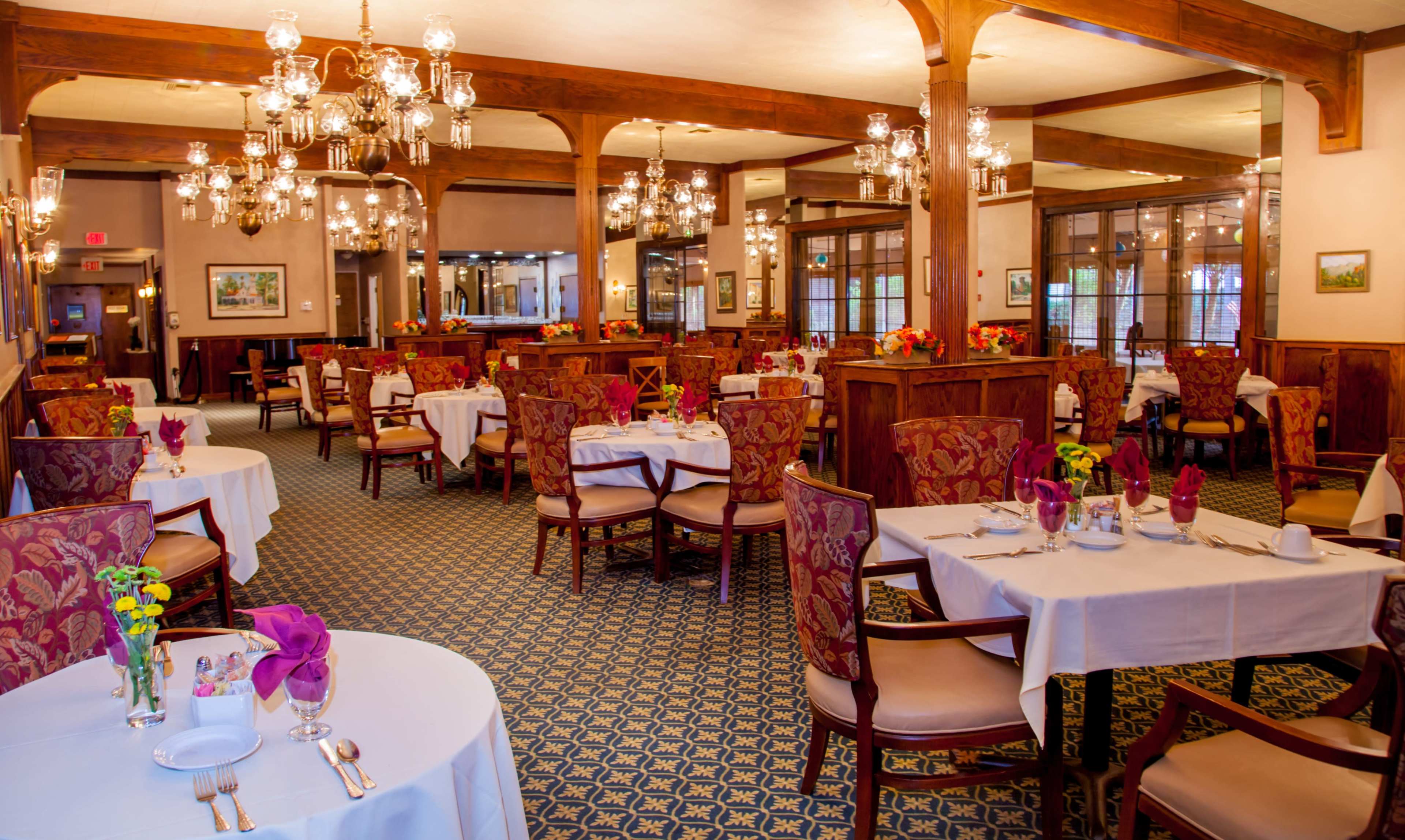 The image shows a spacious restaurant interior with elegantly set tables, wooden beams, and decorative chandeliers.