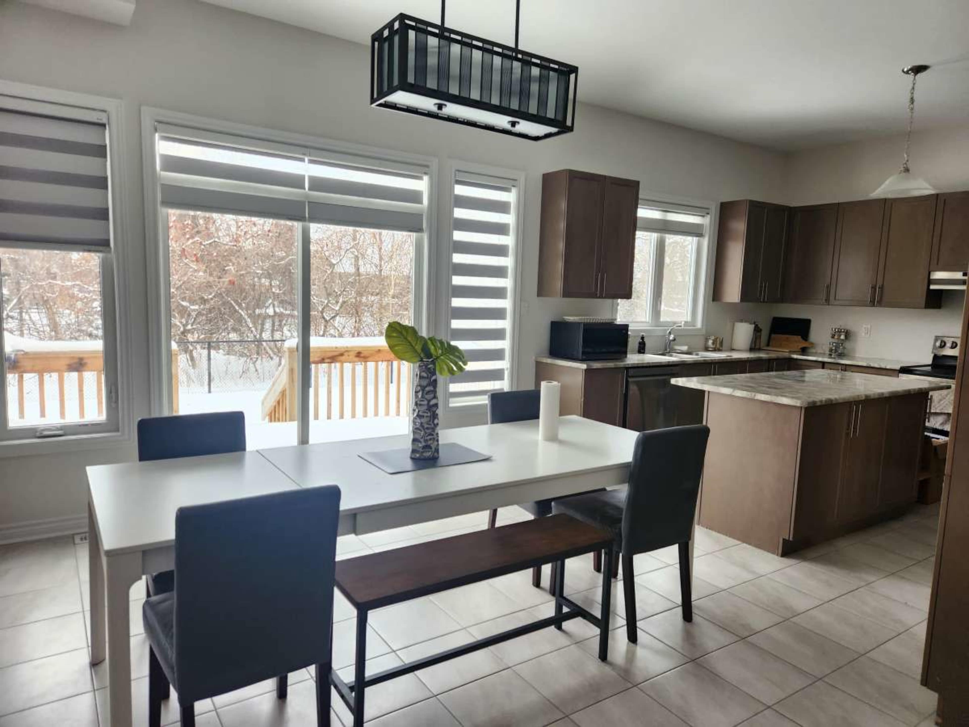 A modern kitchen and dining area features a white table with gray chairs, a bench, and large windows overlooking a snowy landscape.