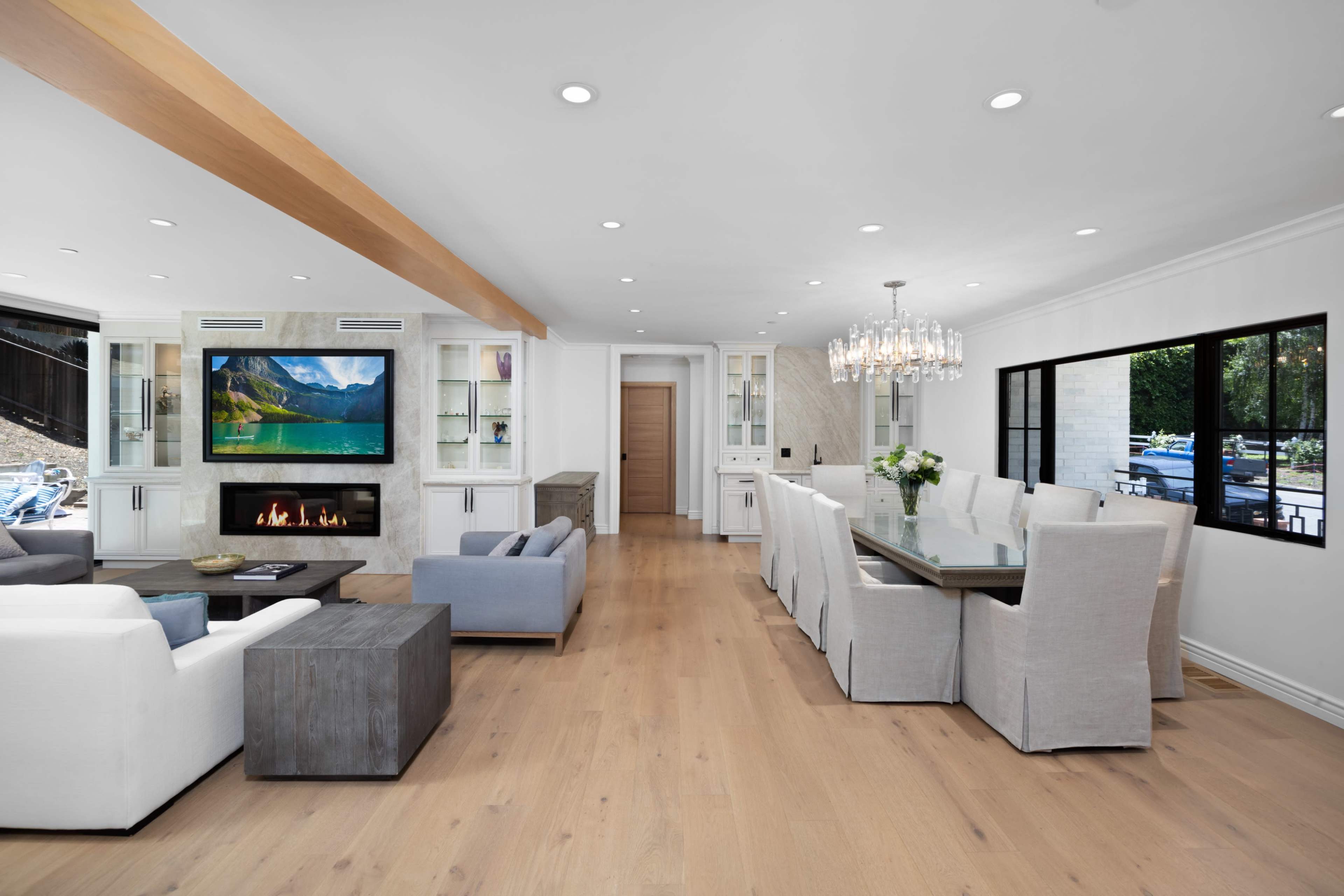 A modern open-concept living and dining area with a fireplace, large television, a dining table, and floor-to-ceiling windows.