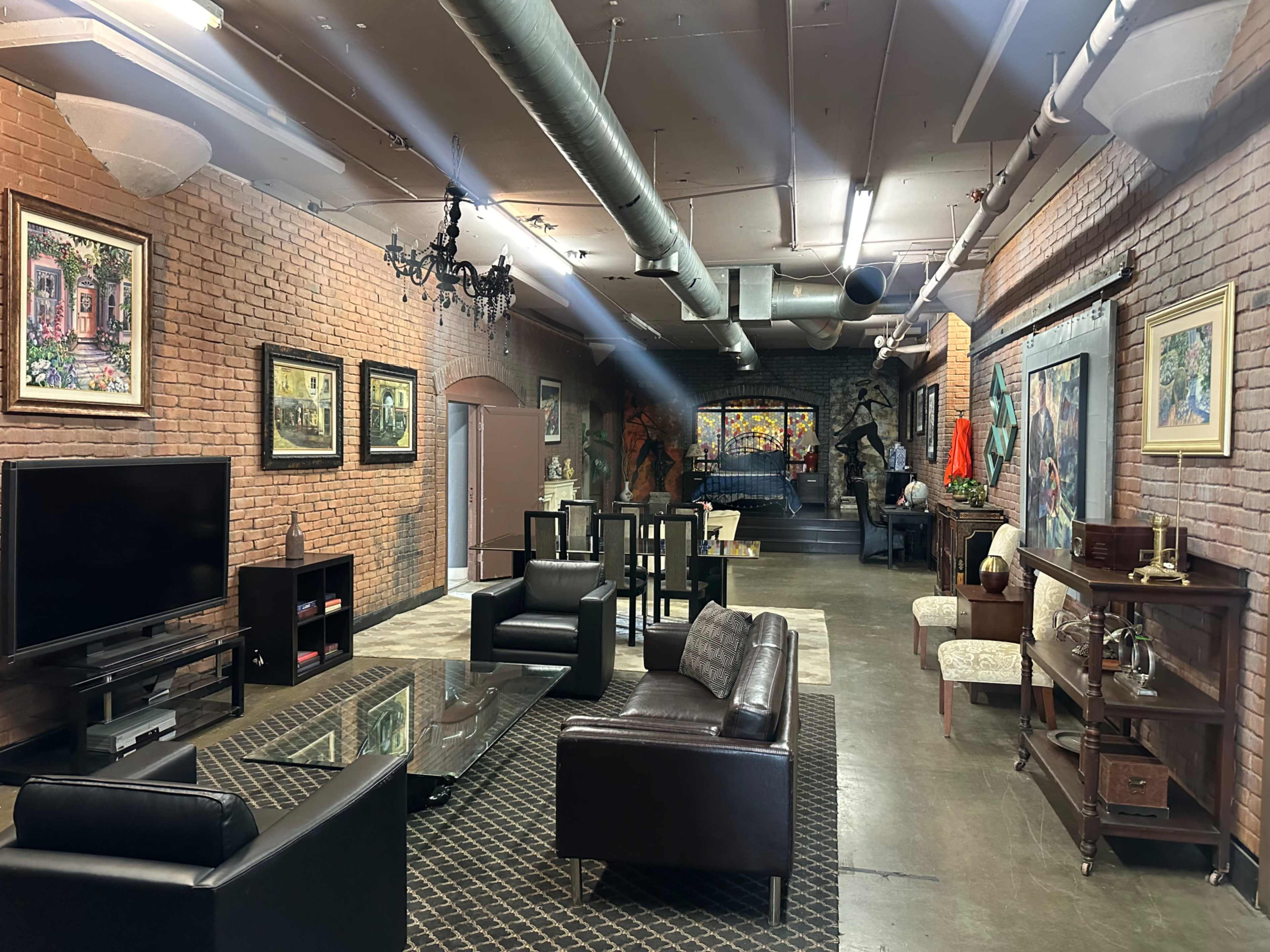A spacious, industrial-style lounge area with exposed brick walls, a television, modern furniture, and various artworks displayed on the walls.