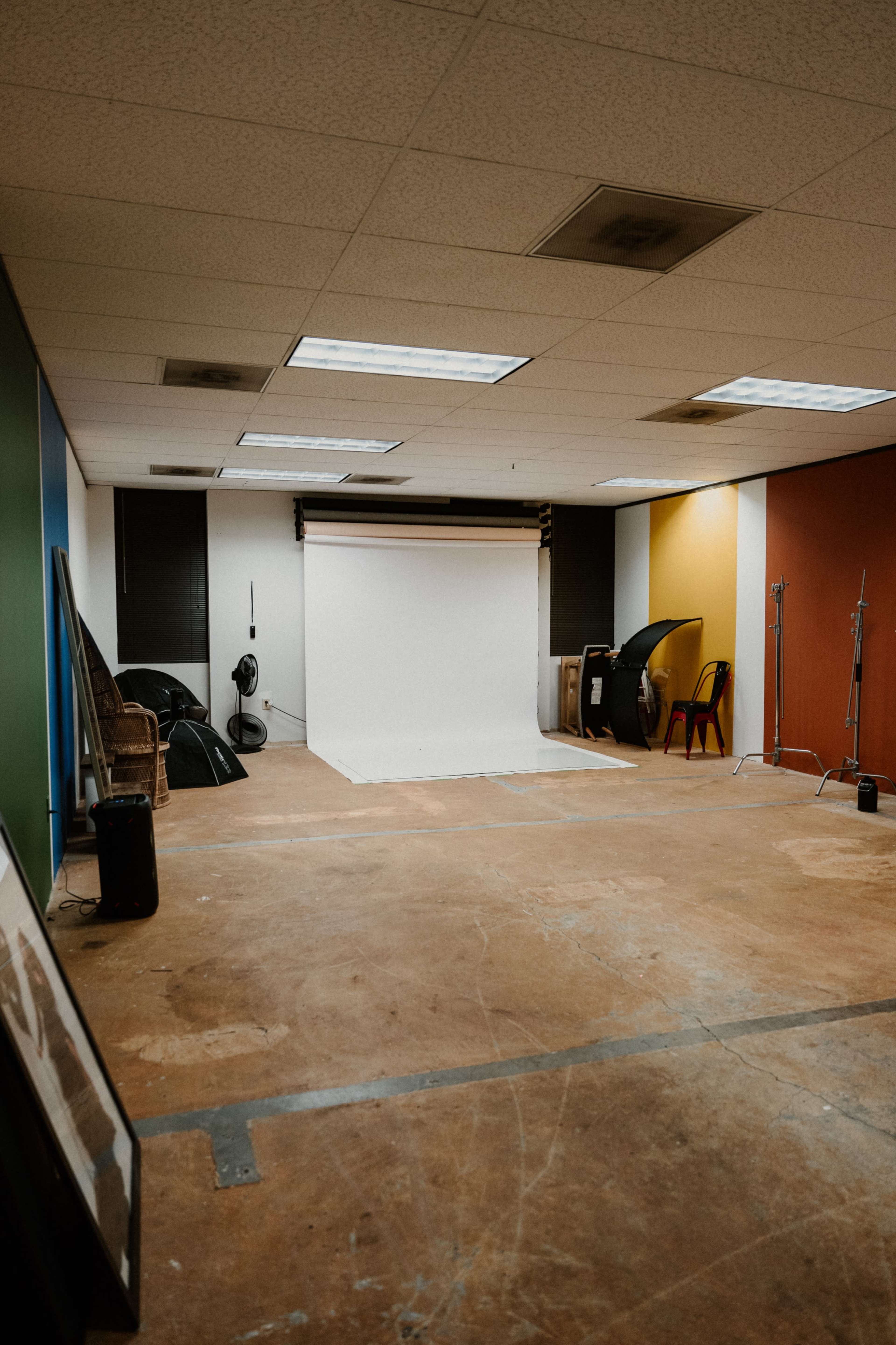 An empty photography studio with a blank backdrop, various lighting equipment, and colorful walls.