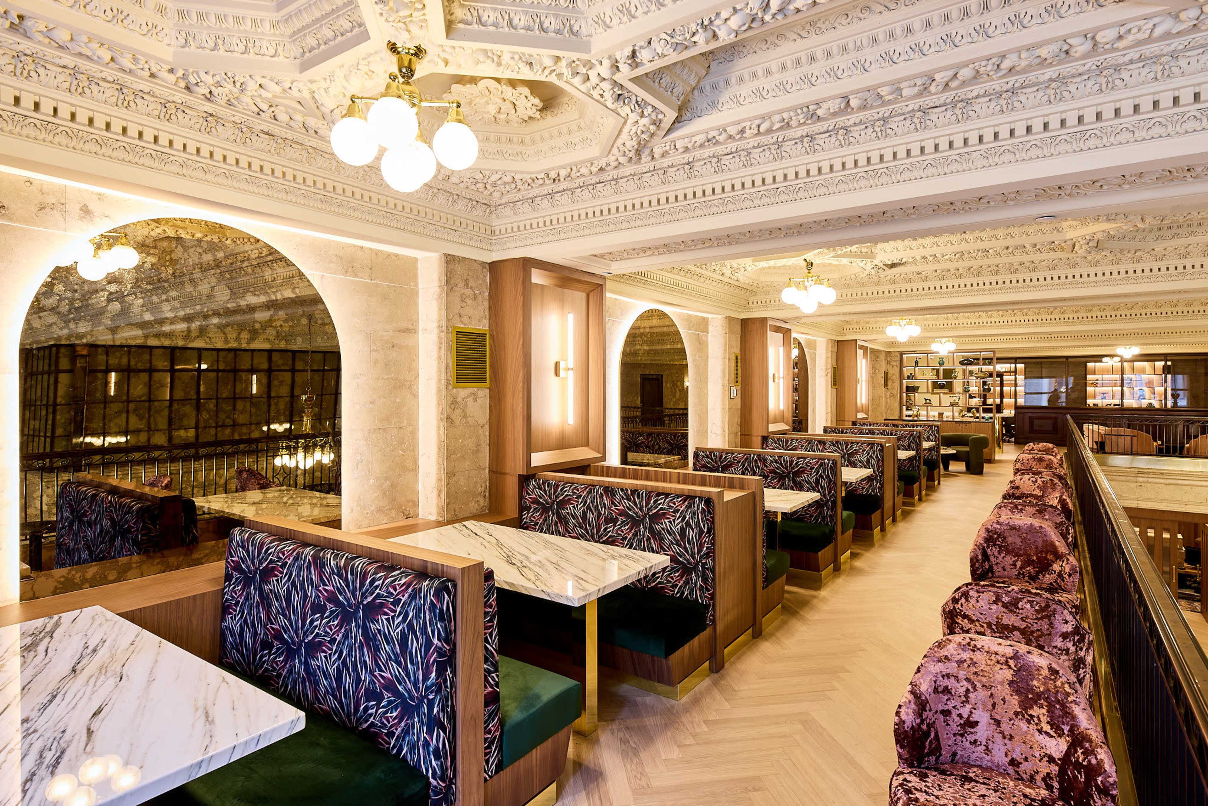 The image shows an elegant dining area in a restaurant featuring ornate ceiling details, arches, and booths with patterned upholstery.