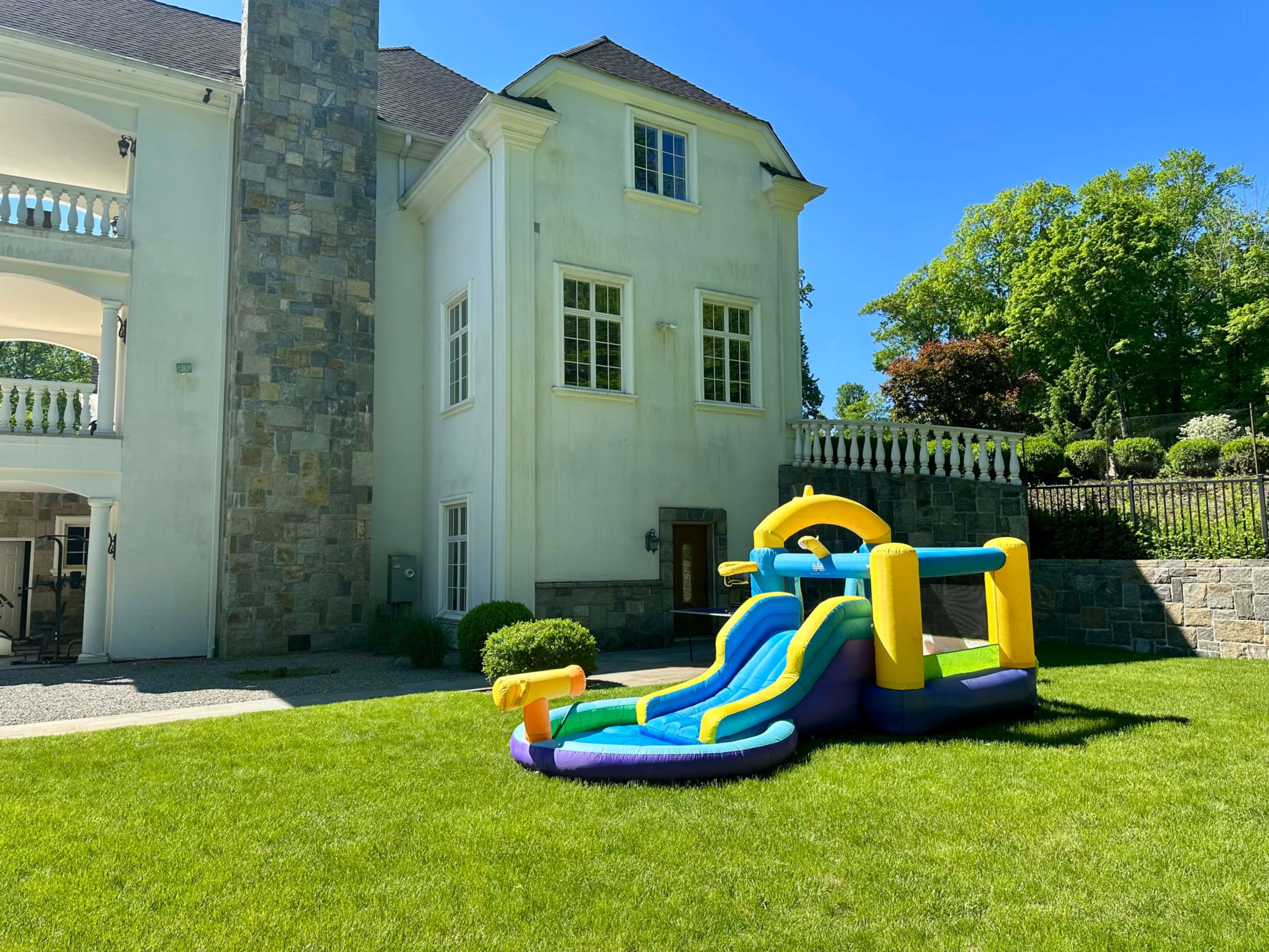 A colorful water slide is set up on the lawn beside a large, modern house.