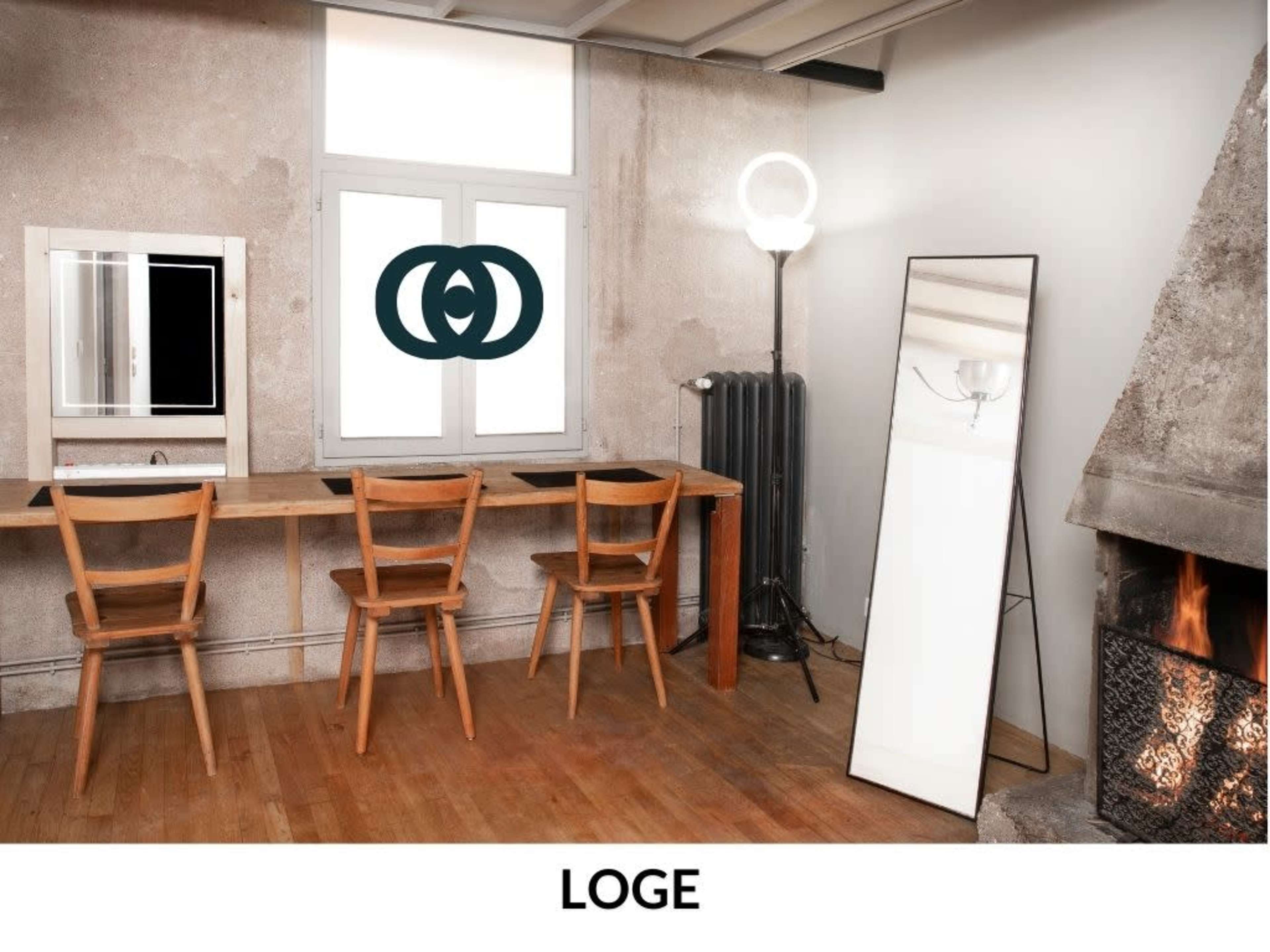 The image shows a minimalist interior with a wooden table featuring three chairs, a large mirror, a floor lamp, and a fireplace in a corner.