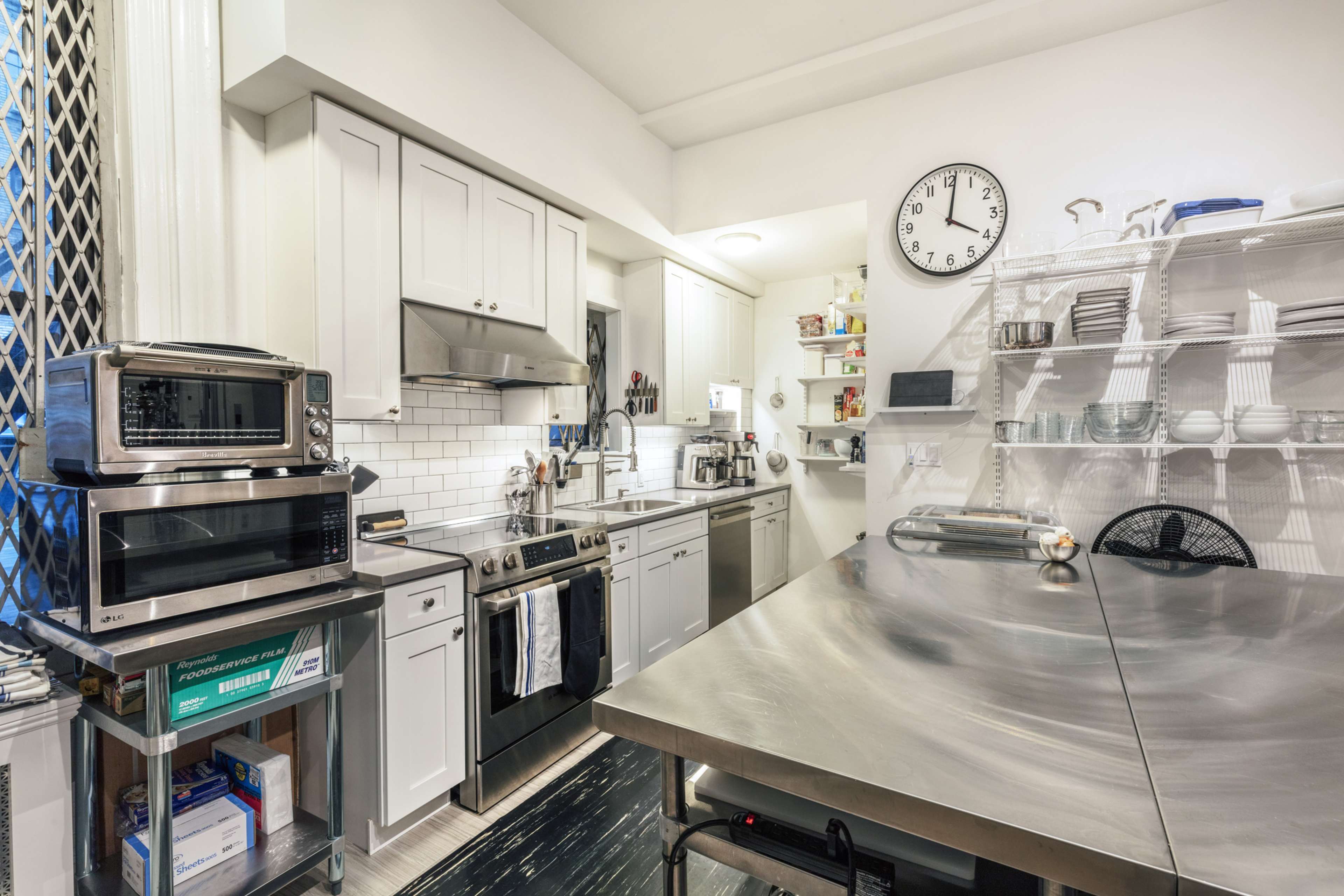 A modern kitchen featuring stainless steel appliances, white cabinets, and a large metal prep table.