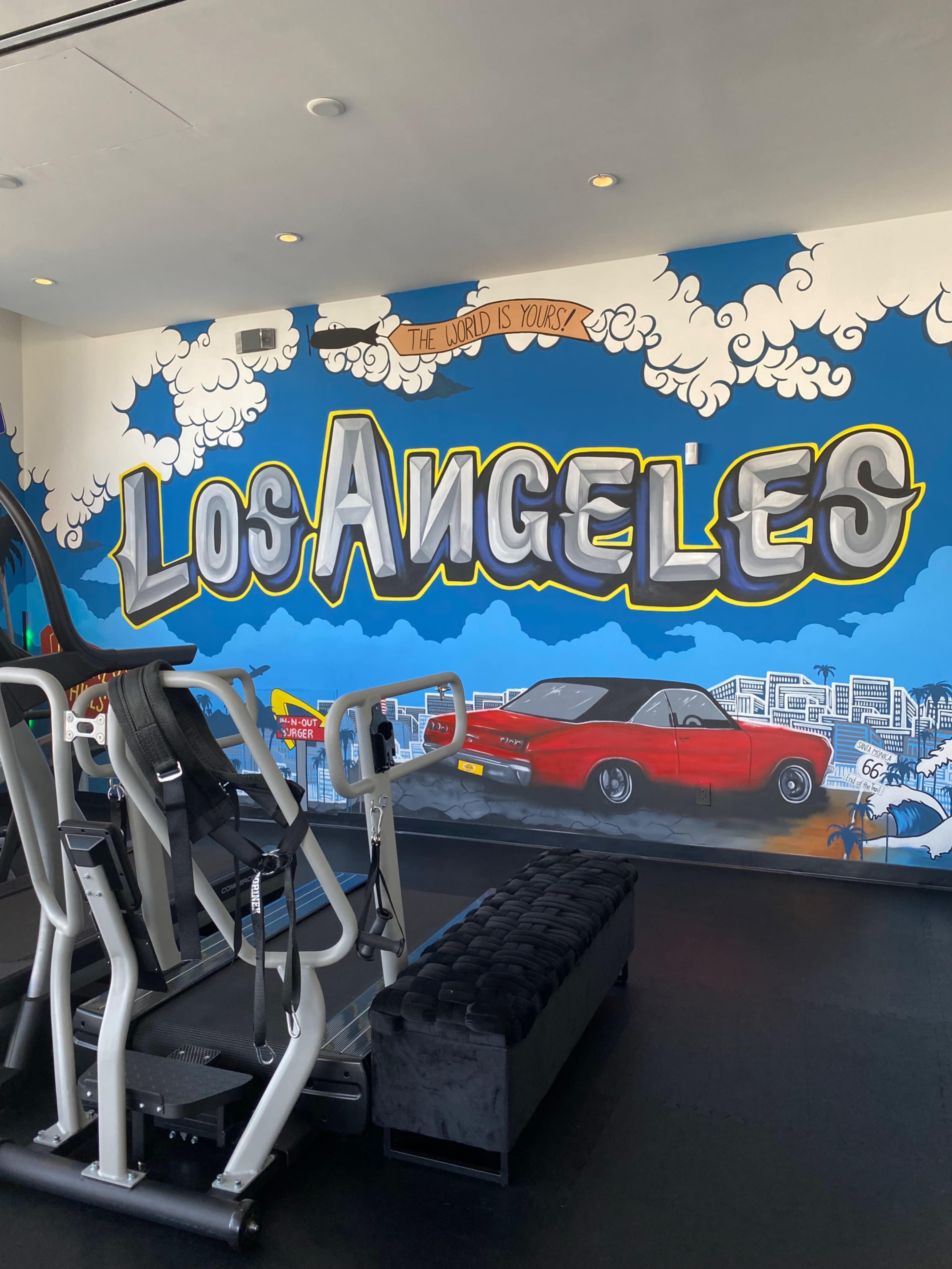 The image shows a gym interior featuring a large mural that reads "Los Angeles" with a vintage car and a cityscape backdrop.