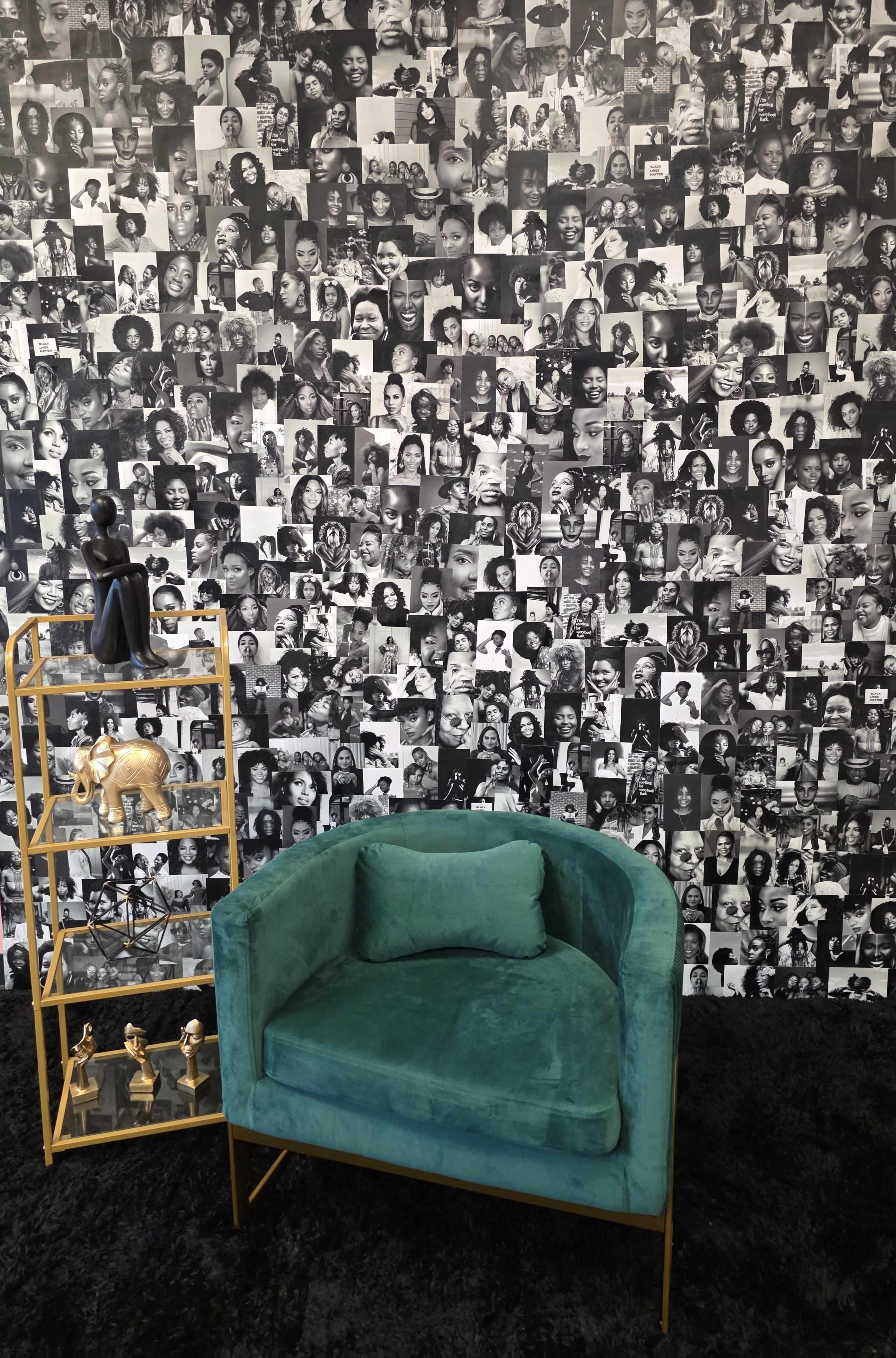 The image features a teal velvet chair in front of a wall covered with a collage of black-and-white photographs of various faces, accompanied by a gold shelving unit displaying decorative items.