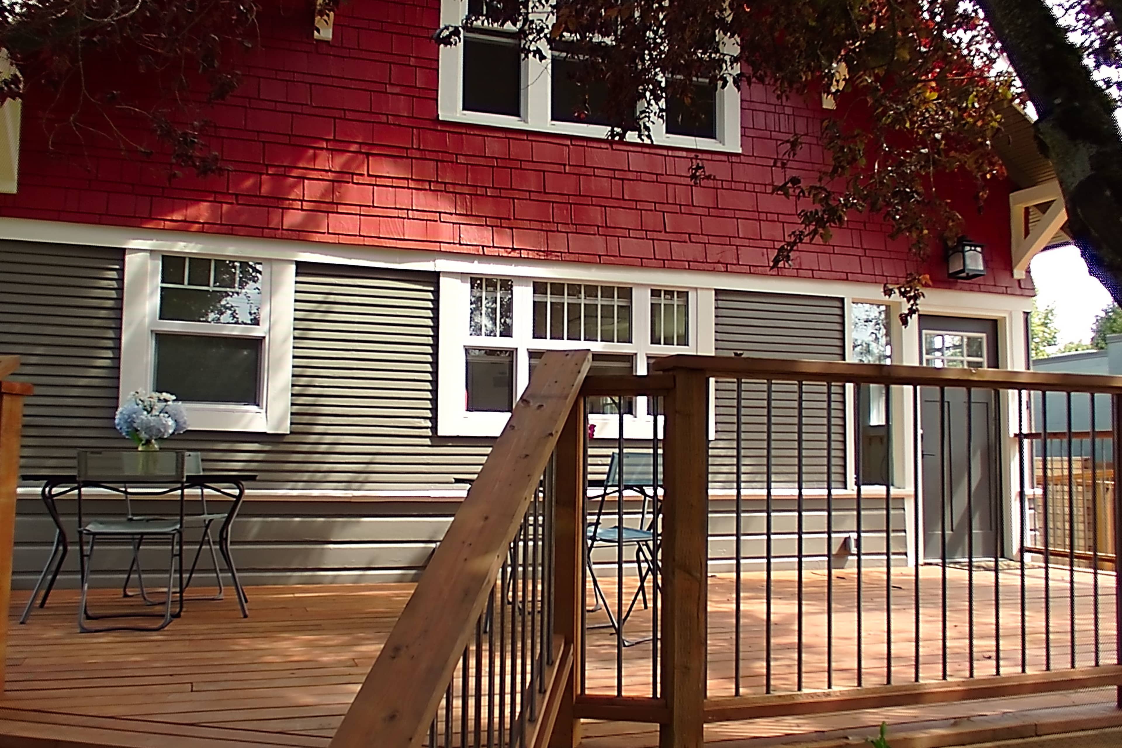 A wooden deck with two black chairs and a small table in front of a red and gray house with multiple windows.