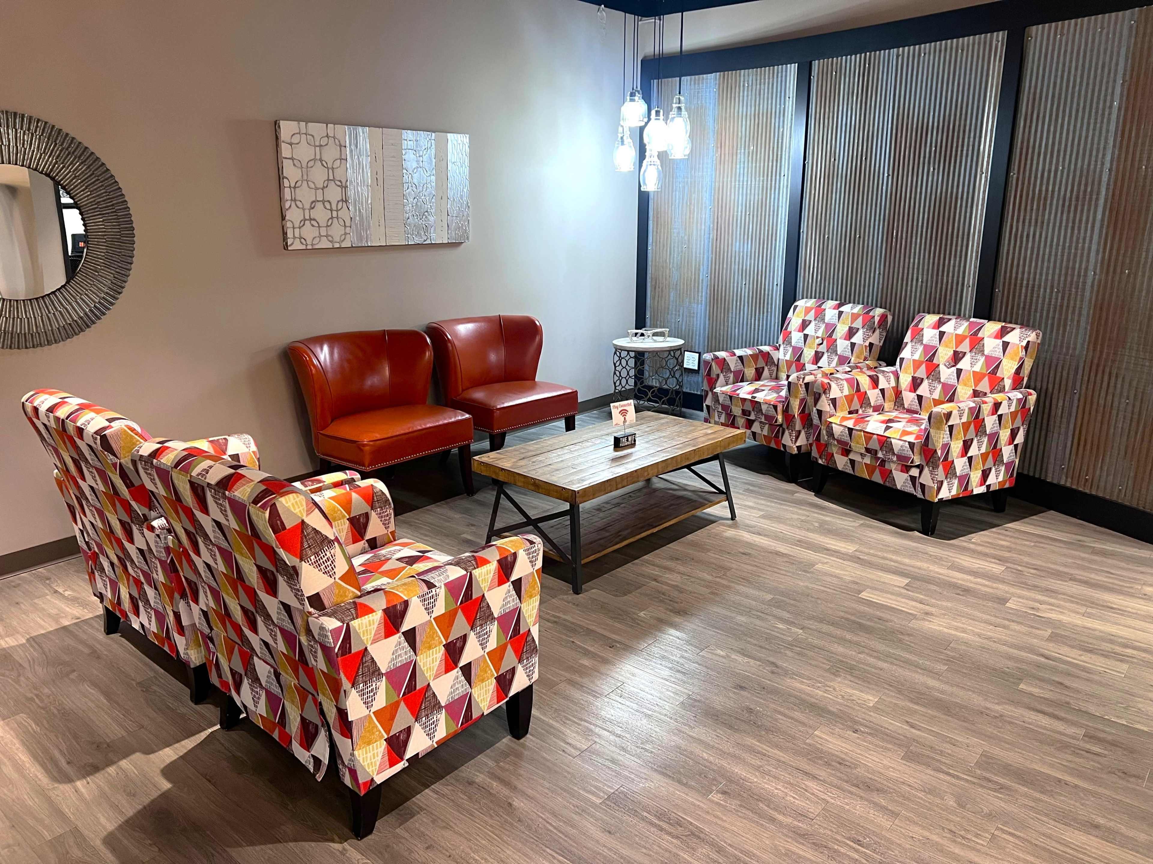 The image shows a seating area with colorful patterned chairs, two red leather armchairs, a wooden coffee table, and decorative wall paneling.