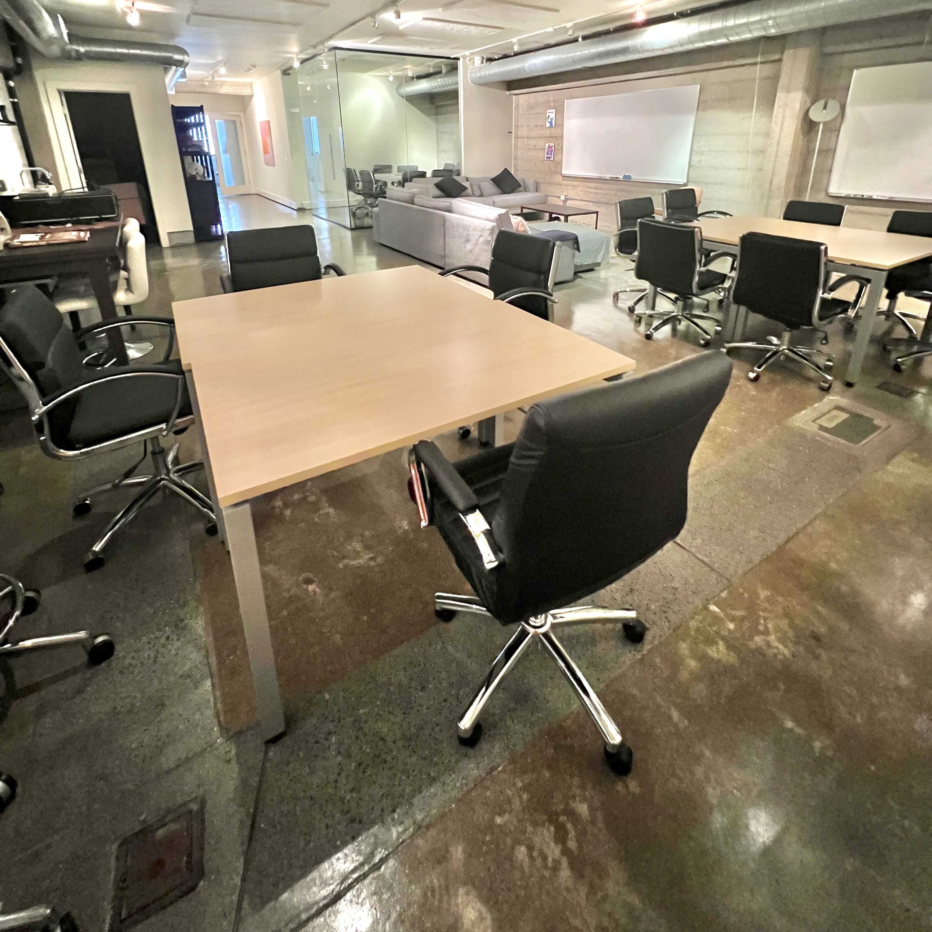 An office space features several black ergonomic chairs and wooden tables arranged in a modern setting with concrete walls.