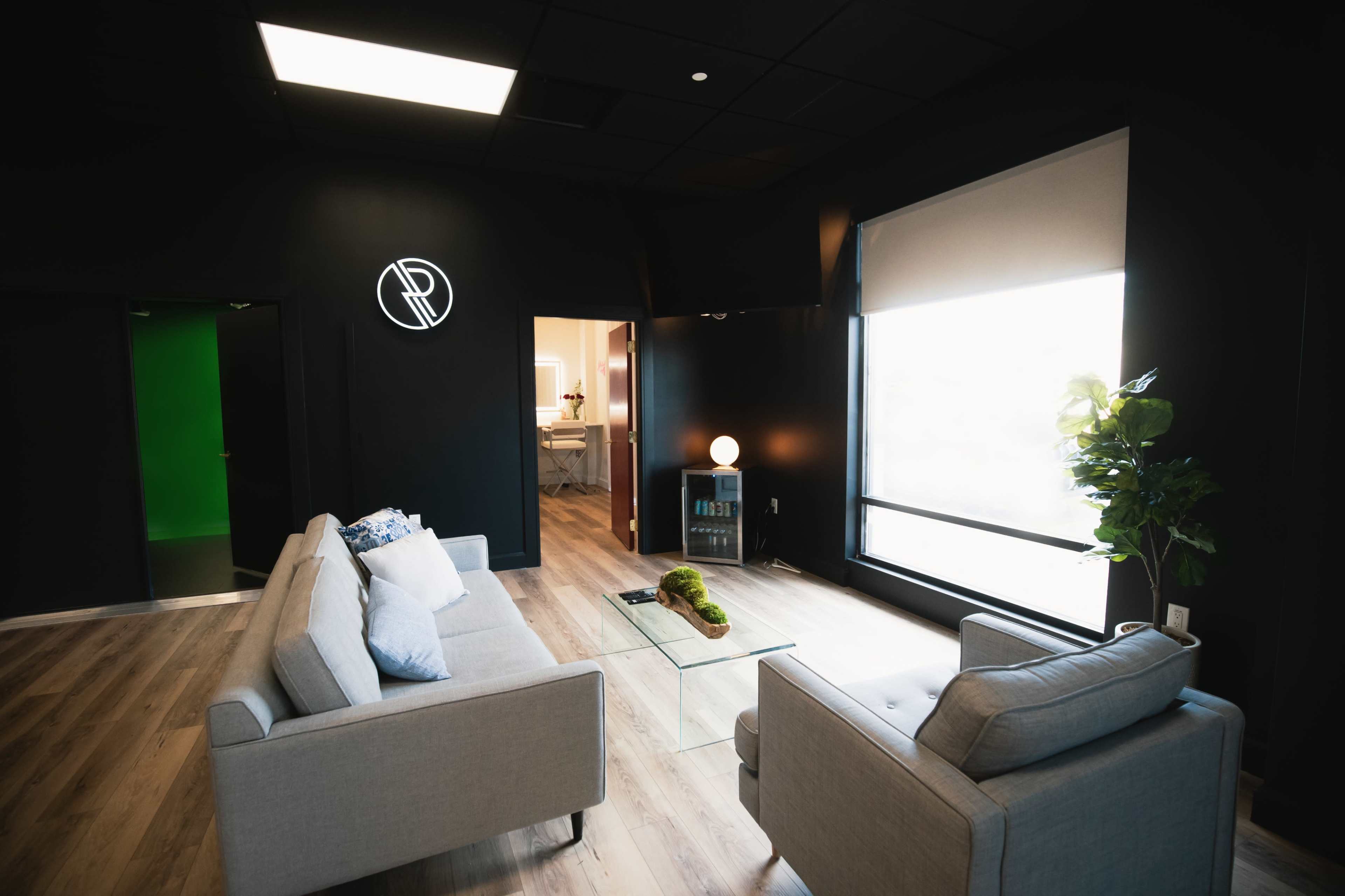 A modern office lounge area with two gray sofas, a glass coffee table, and a large window letting in natural light.