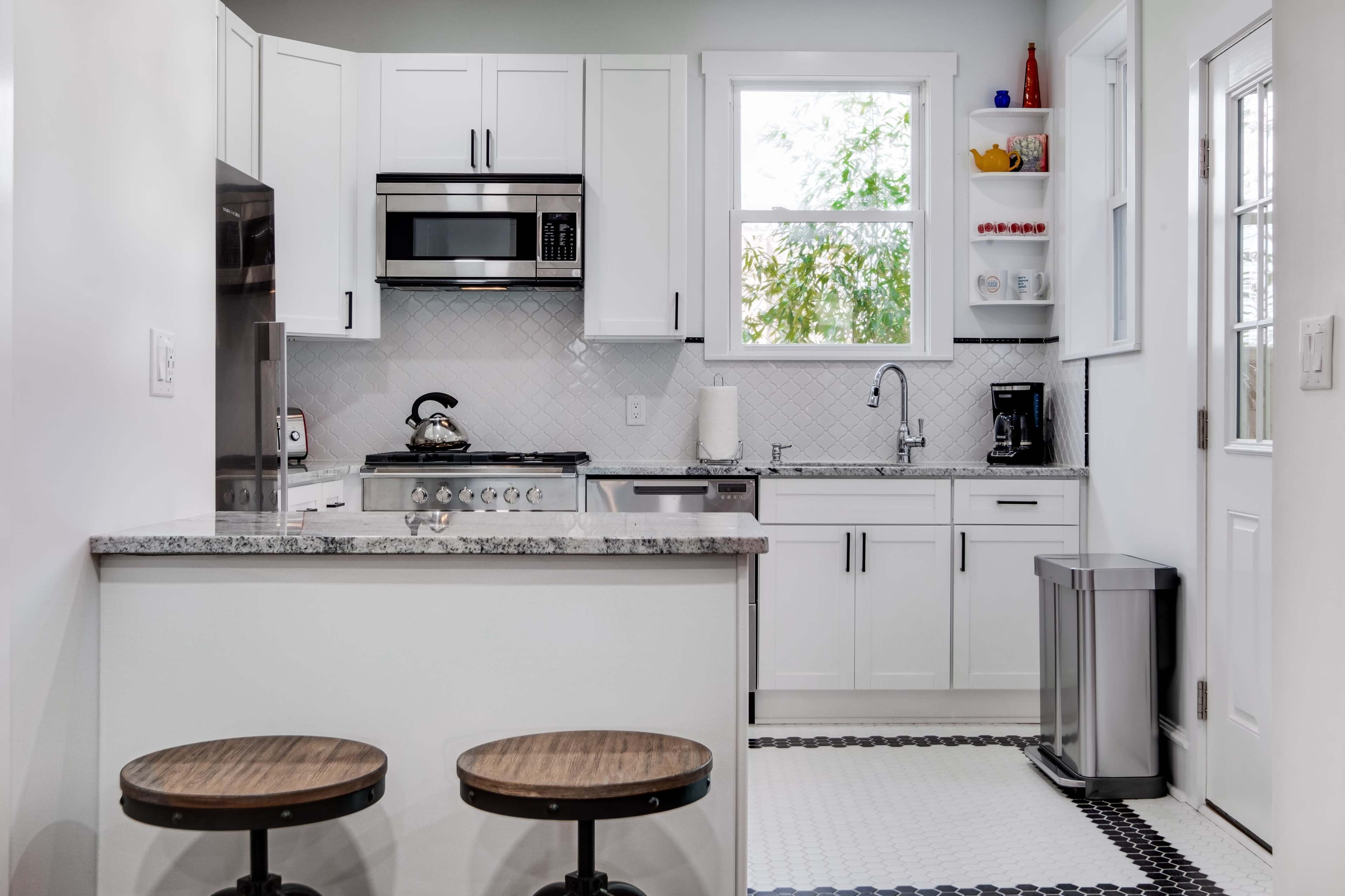 A modern kitchen features white cabinets, stainless steel appliances, and a window overlooking greenery.