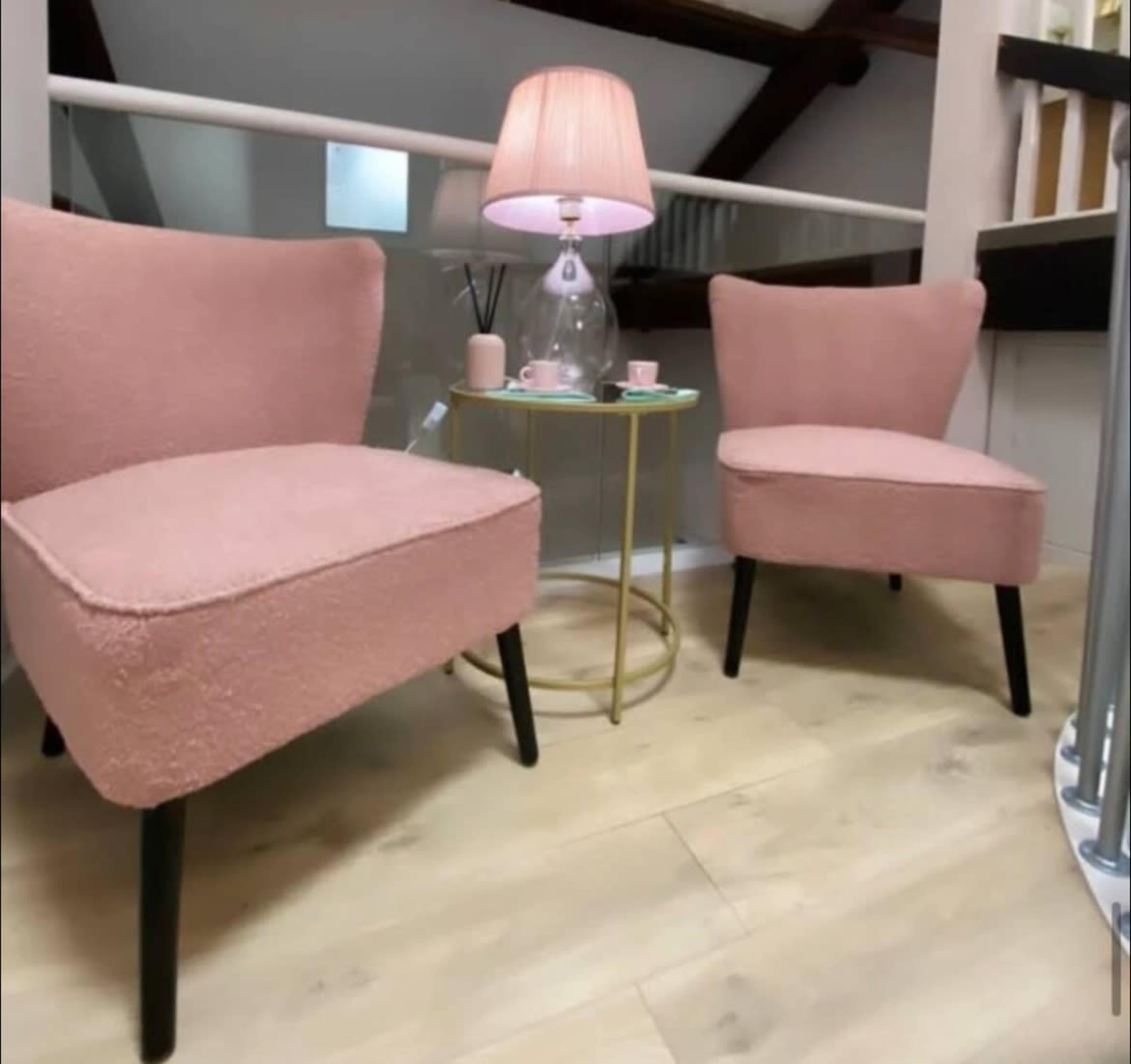 The image shows two pink chairs positioned around a small round table with a lamp and cups on it in a well-lit interior space.