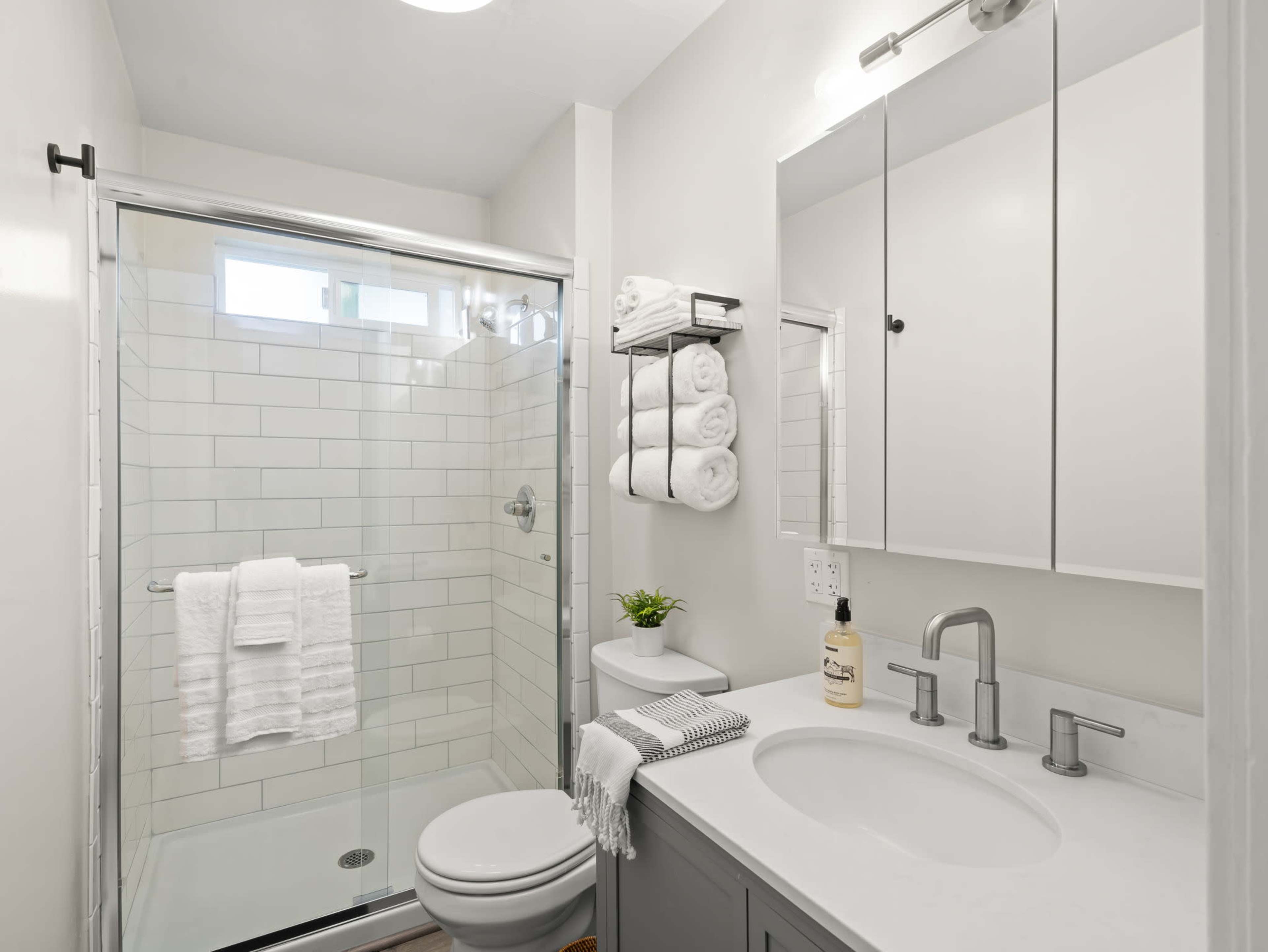 A modern bathroom featuring a glass shower, a white sink with two faucets, and neatly arranged towels on a rack.