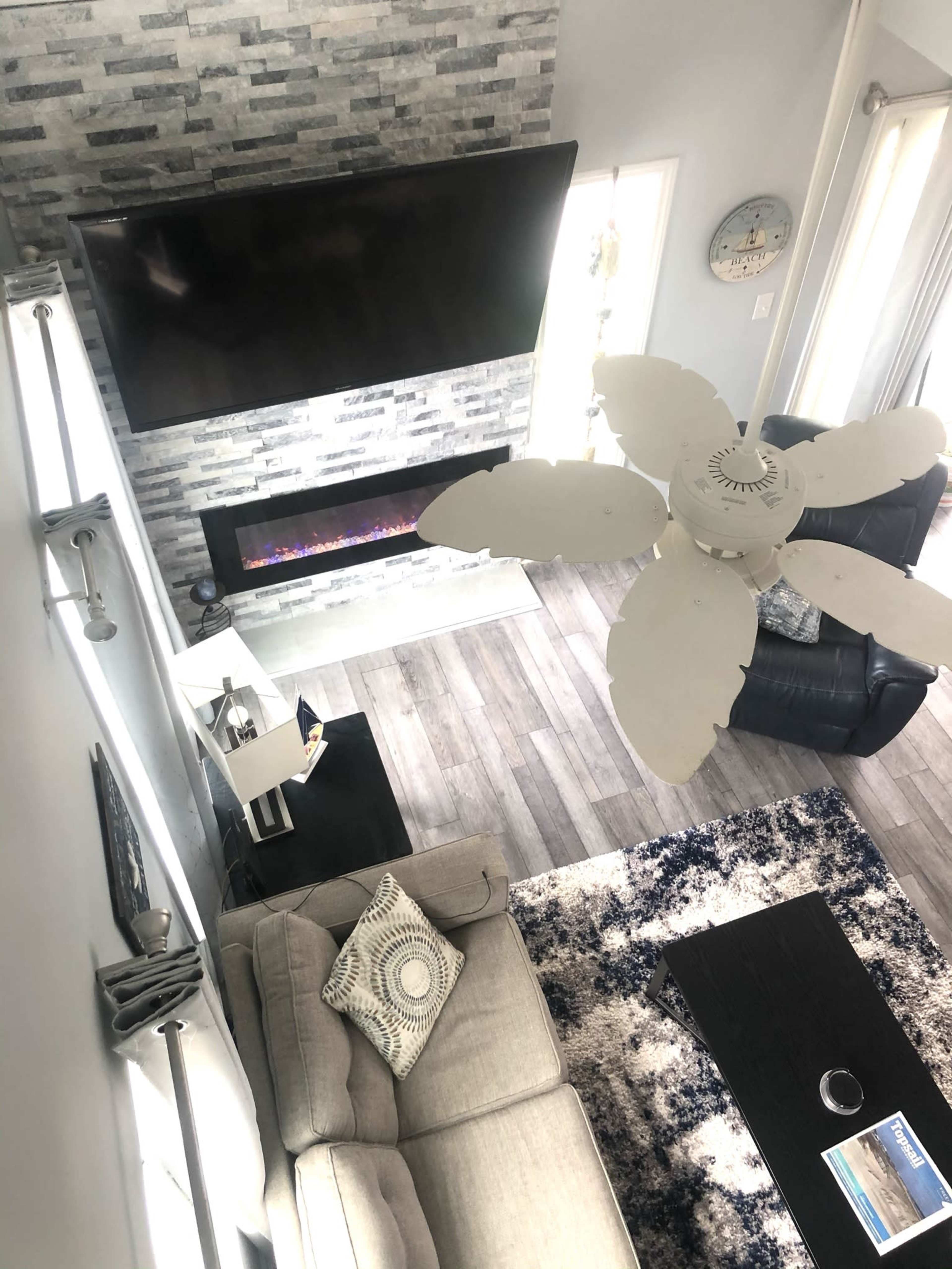 The image shows a modern living room with a stone accent wall, an electric fireplace beneath a large television, and seating arrangements including a sectional sofa and leather armchairs.