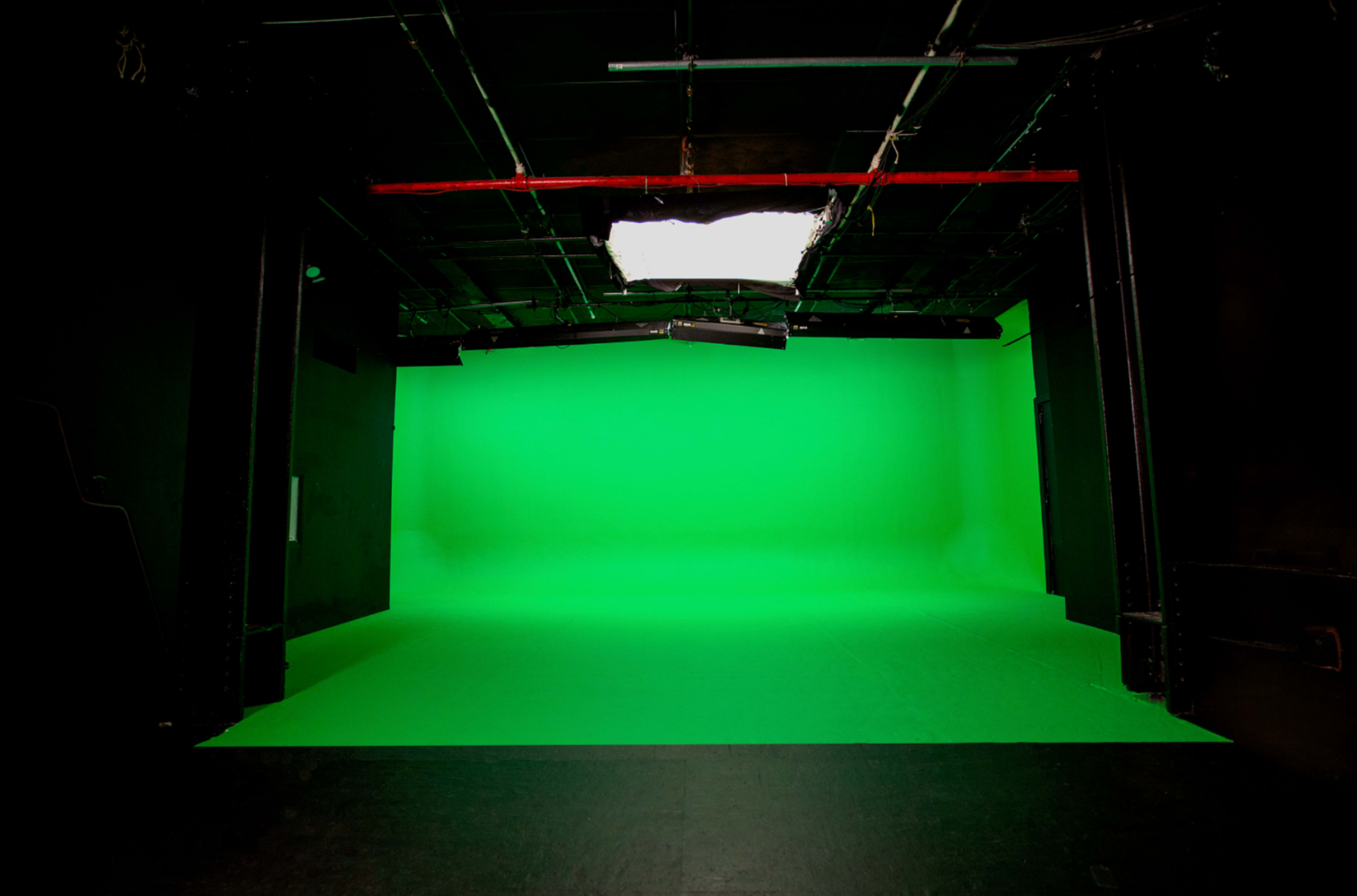 The image shows an empty studio with a bright green backdrop and dim overhead lighting.