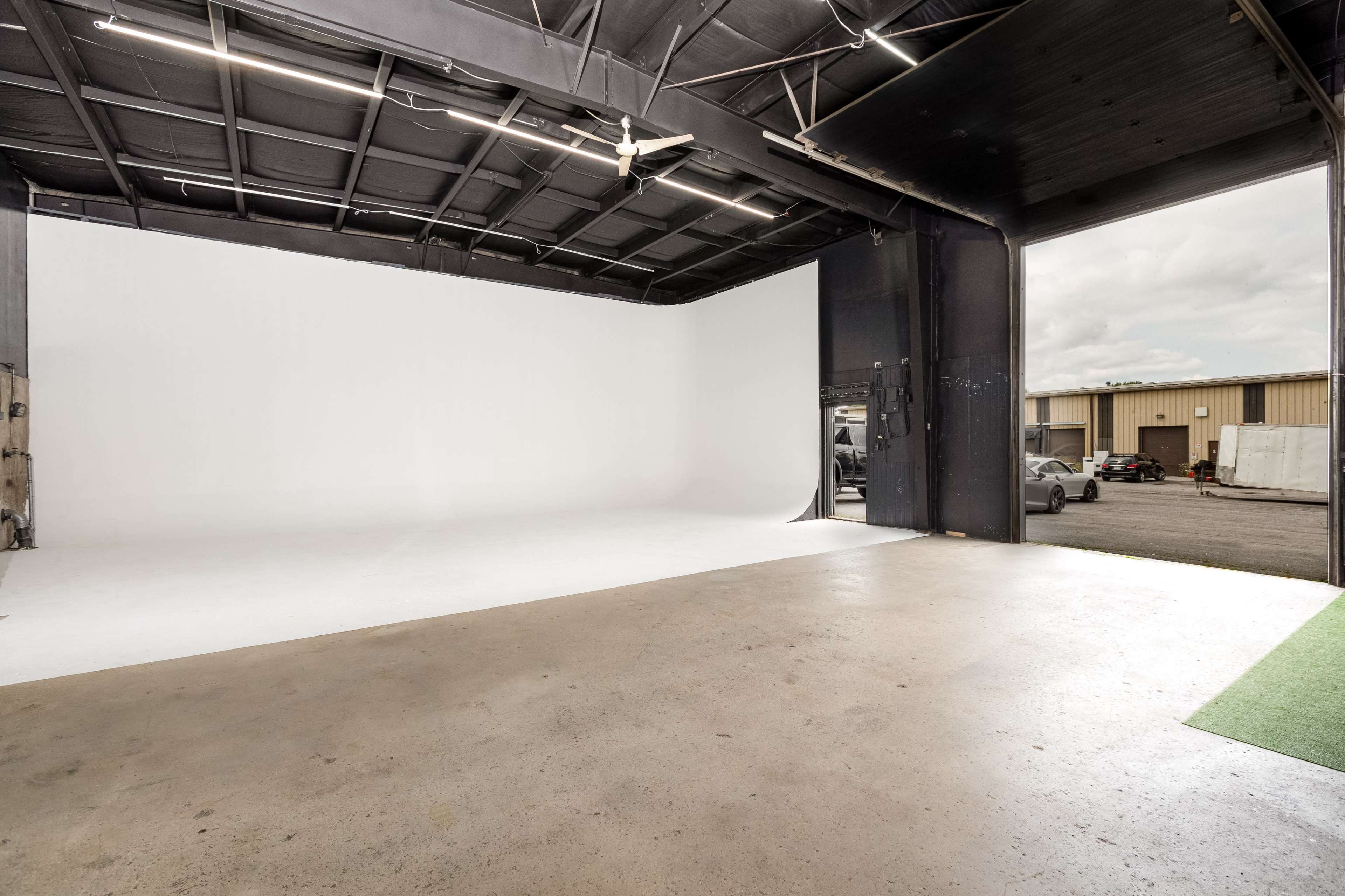 A spacious photo studio with a seamless white backdrop and an open garage door leading to an outdoor area.