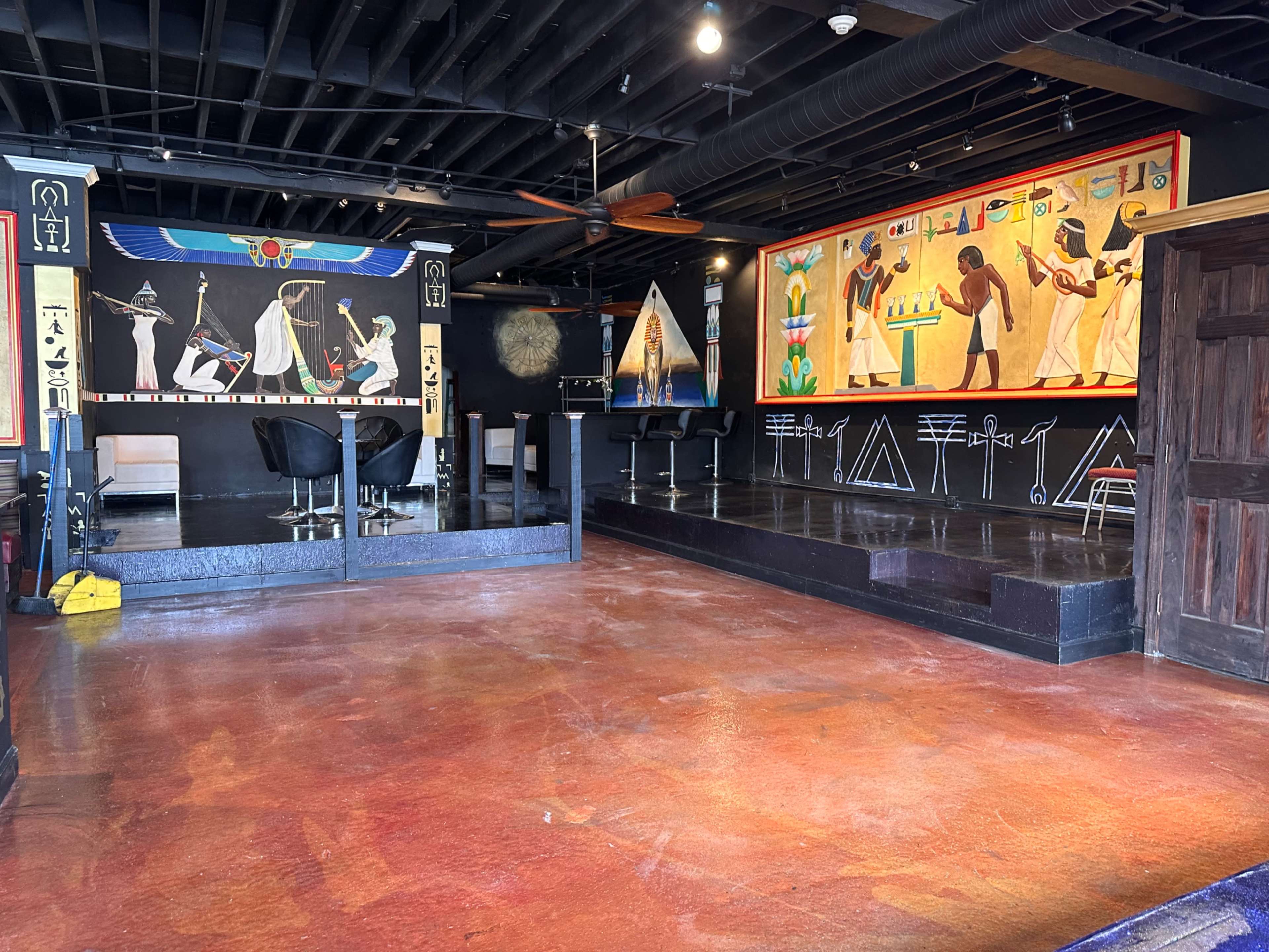 The interior features a spacious room with vibrant murals depicting ancient Egyptian themes on the walls and a polished concrete floor.