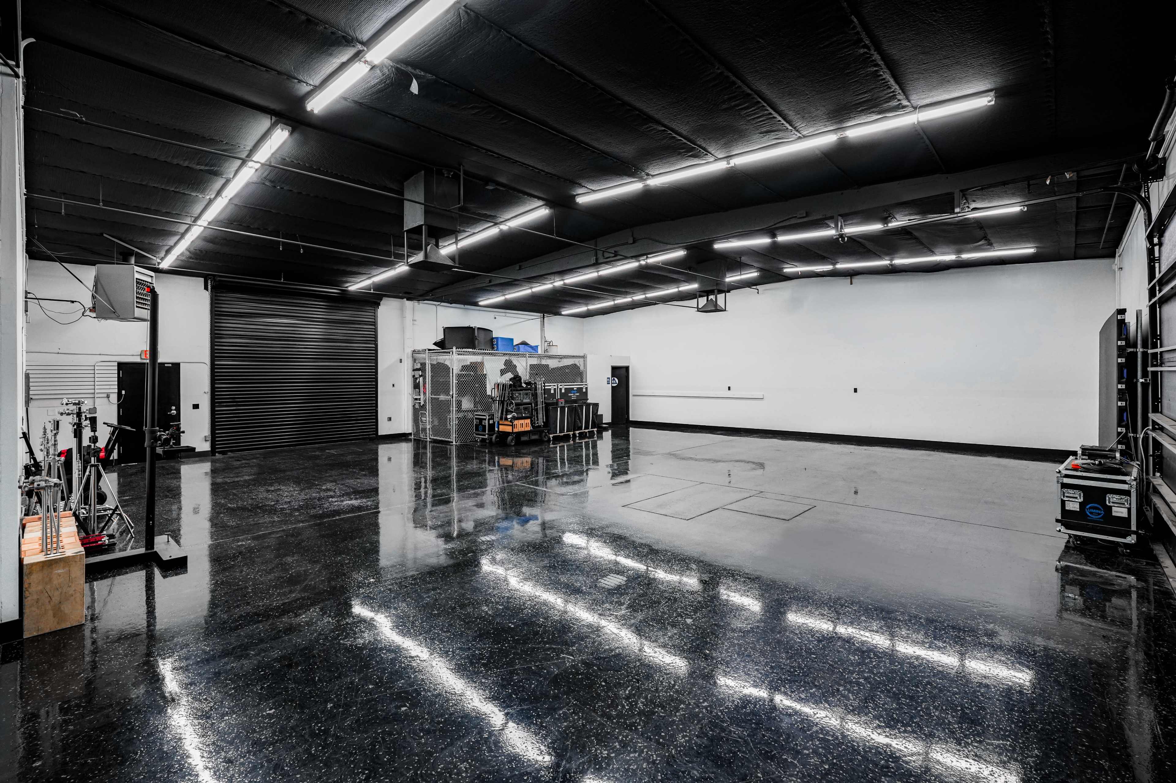 The image shows an empty industrial space with a polished black floor, fluorescent lighting, and various equipment along the walls.