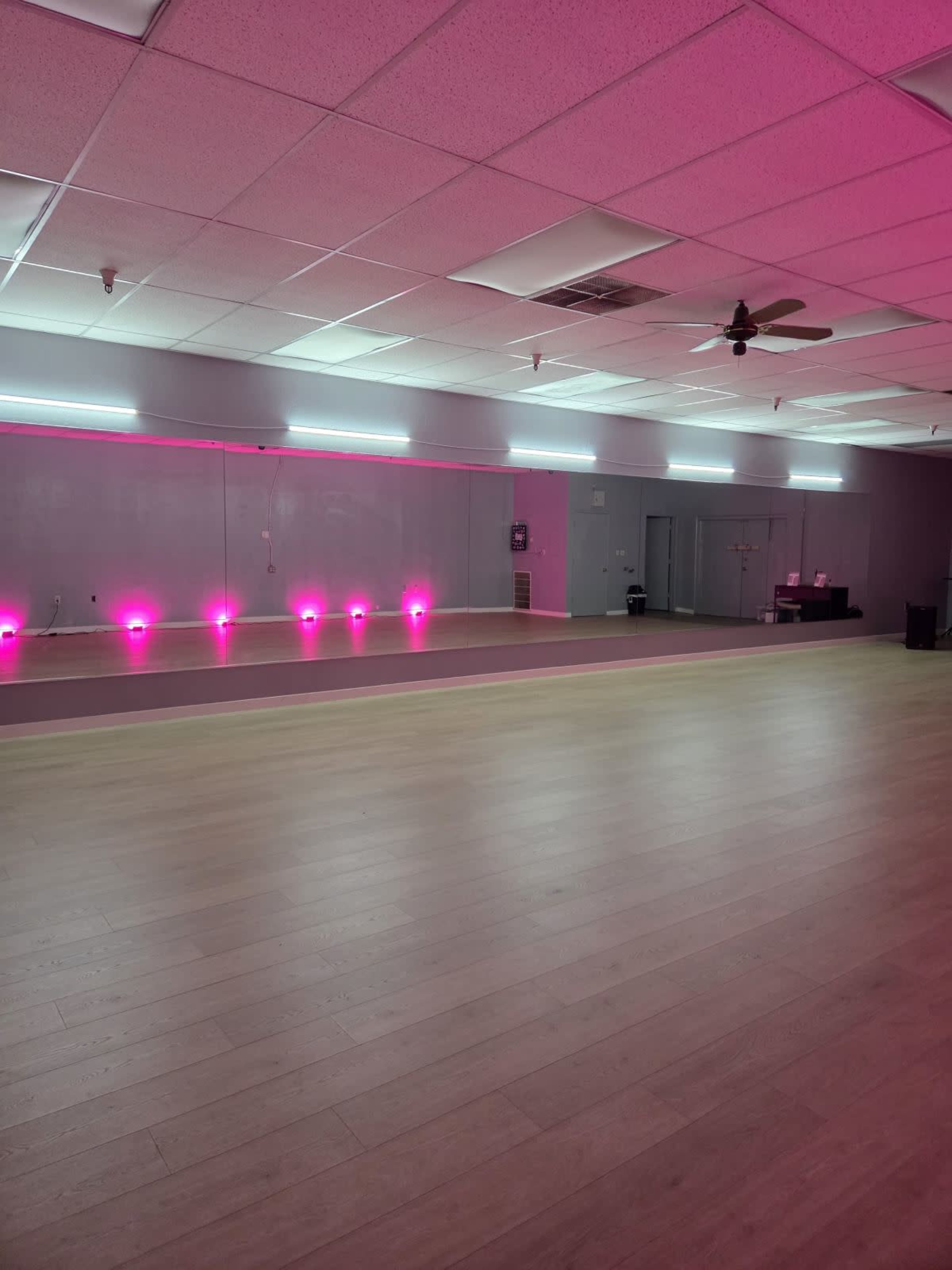 The room features a spacious wooden floor with pink neon lighting along the walls and a fan on the ceiling.