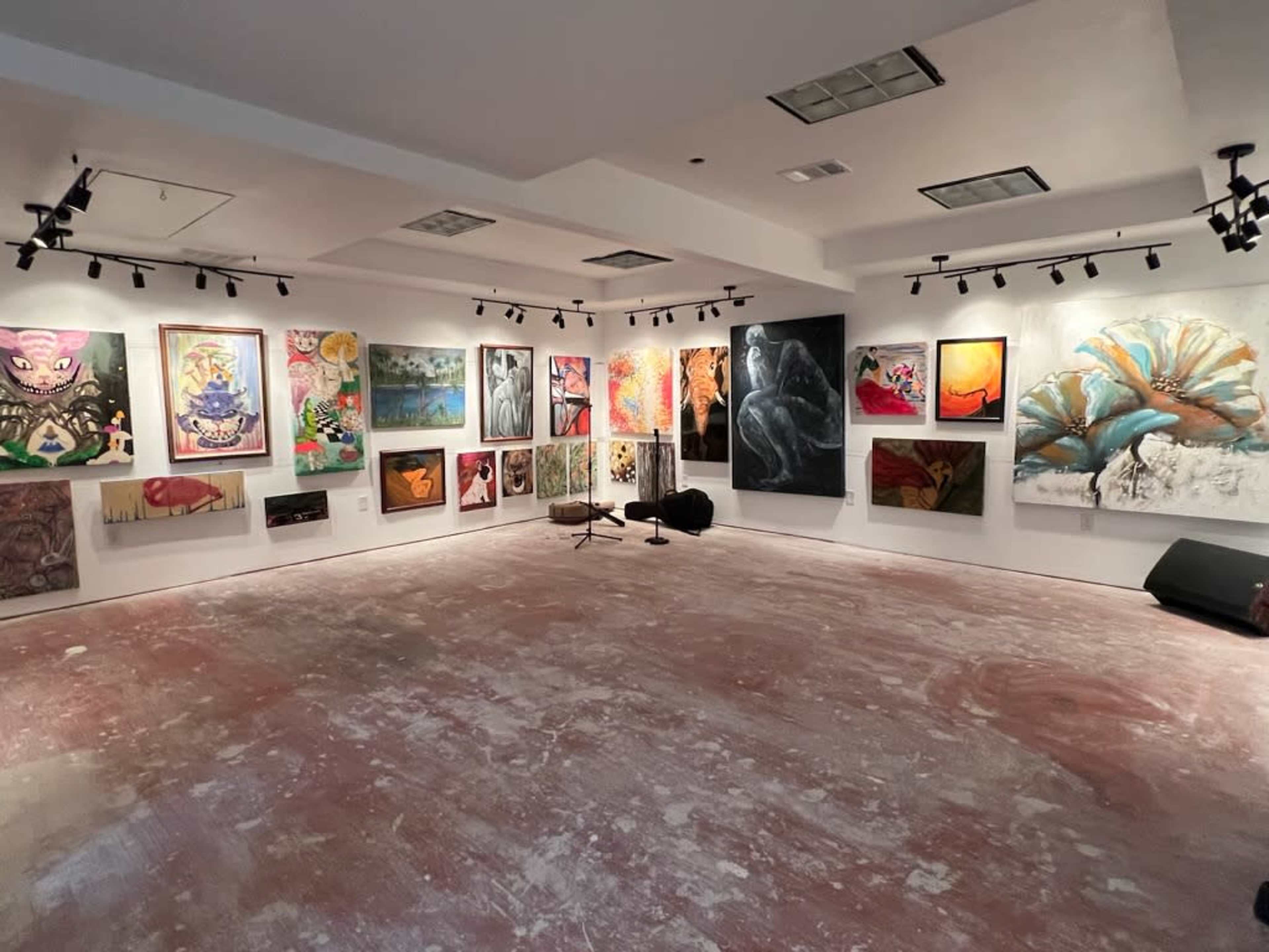 An art gallery with various paintings displayed on the walls and a bare floor.