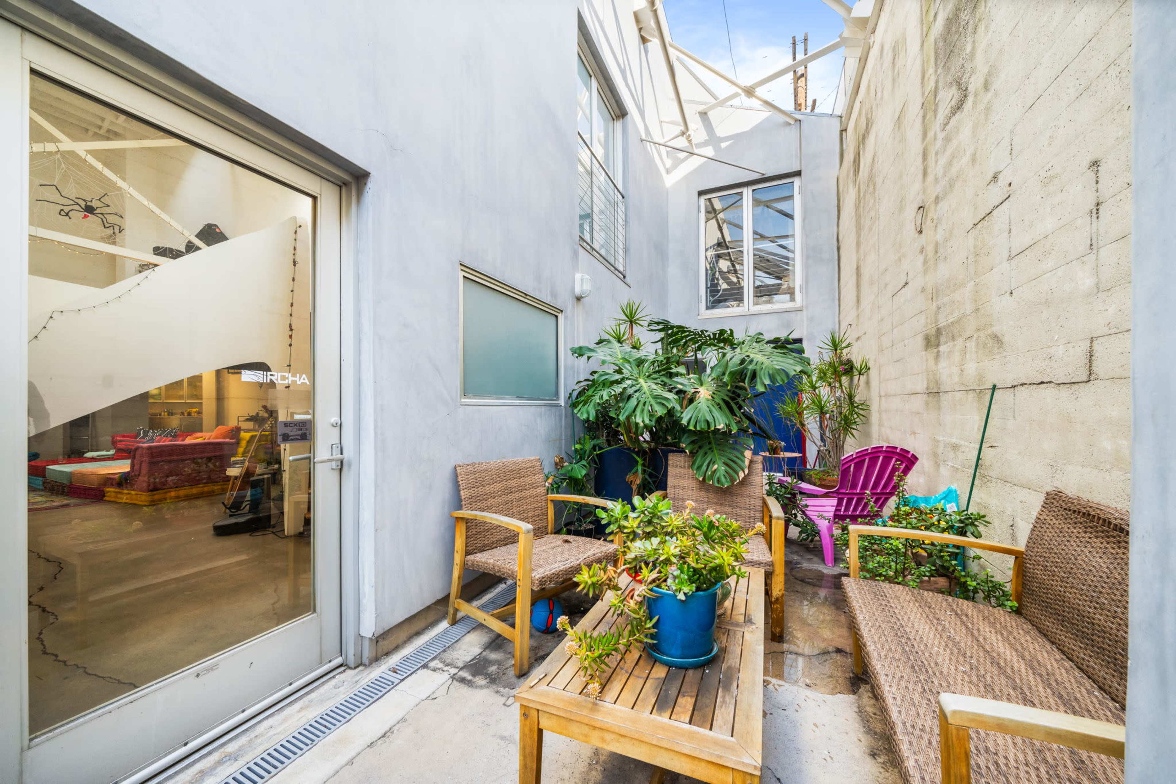 A small outdoor patio area with wooden furniture, surrounded by walls and various potted plants.