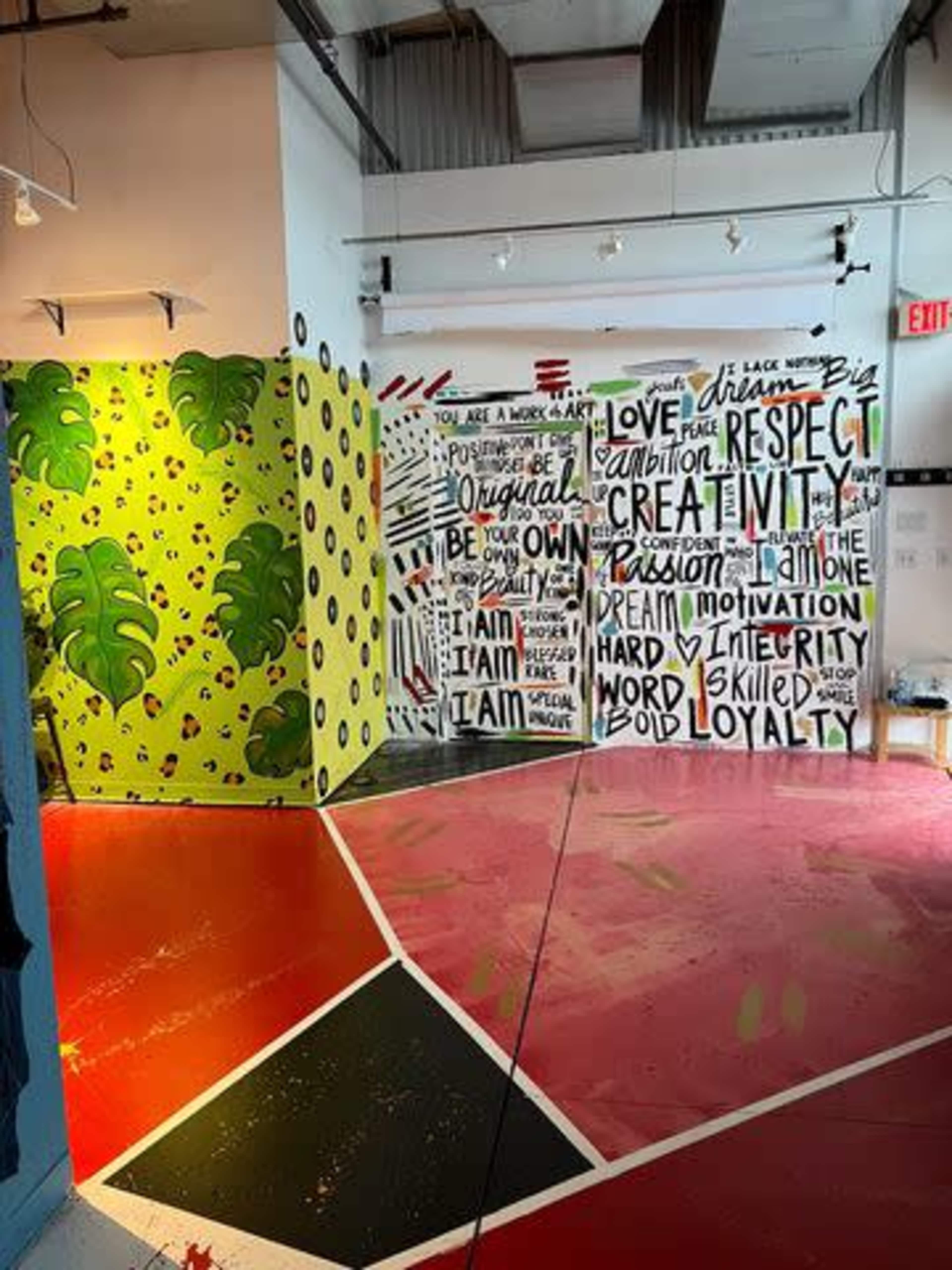 An interior space with vibrant murals and painted walls displaying motivational words and colorful leaf patterns on the opposite wall.