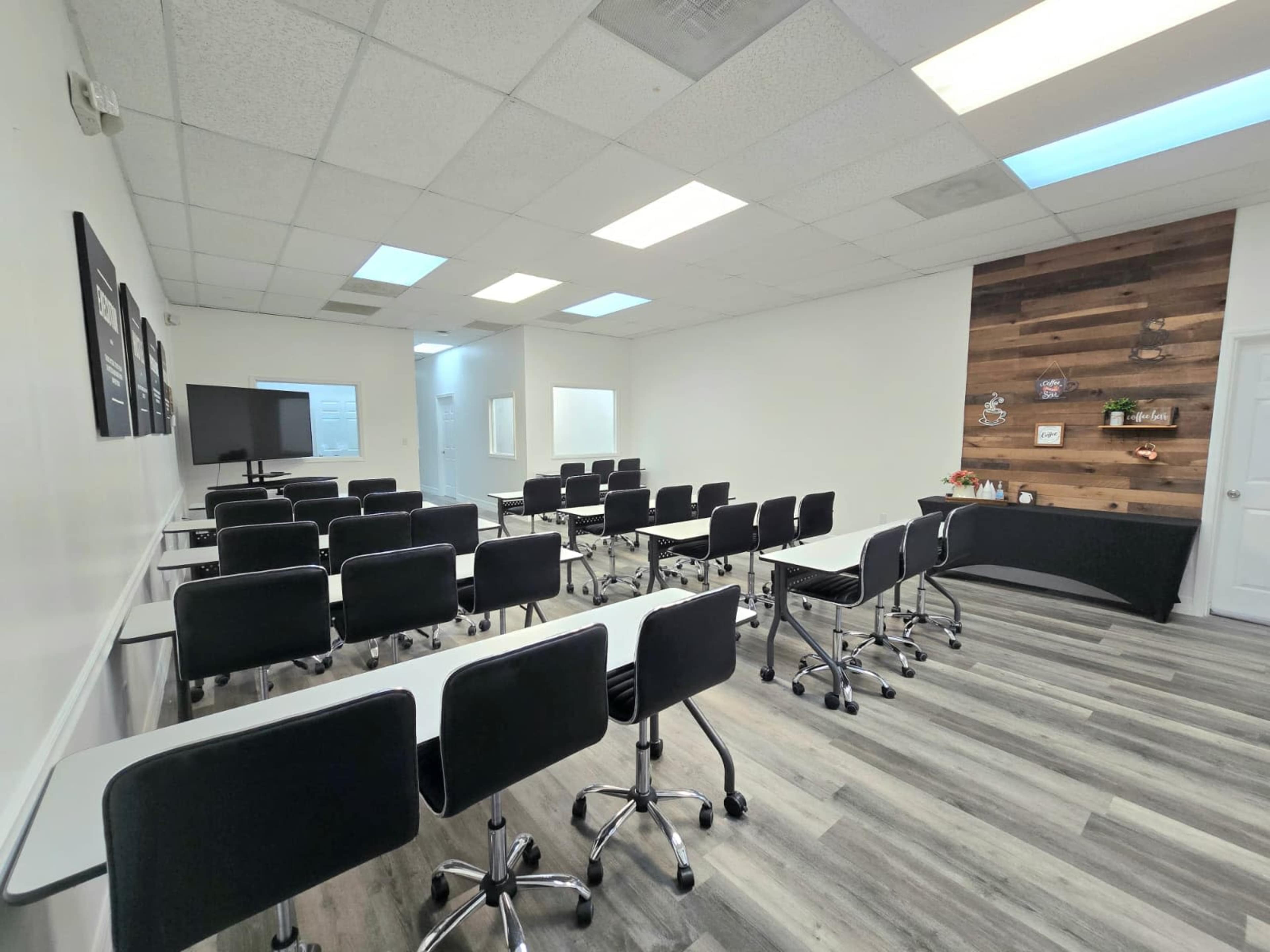 The image shows a modern classroom setup with rows of black chairs and tables, a projector screen, and a wooden feature wall.