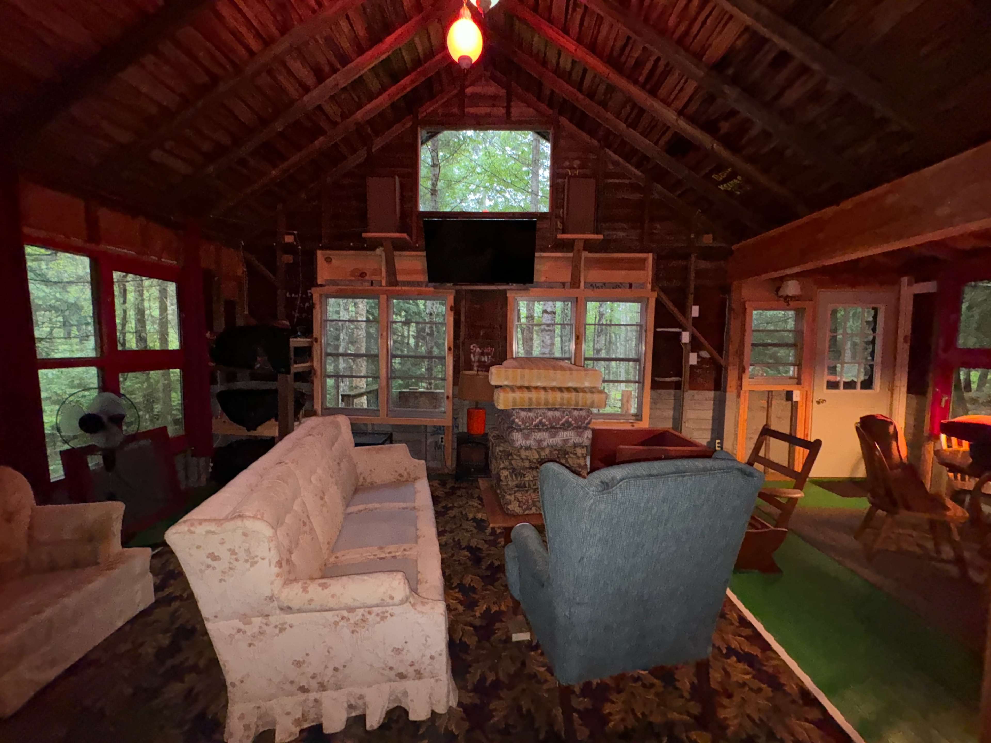 The interior of a rustic cabin features comfortable seating and large windows that offer a view of the surrounding forest.