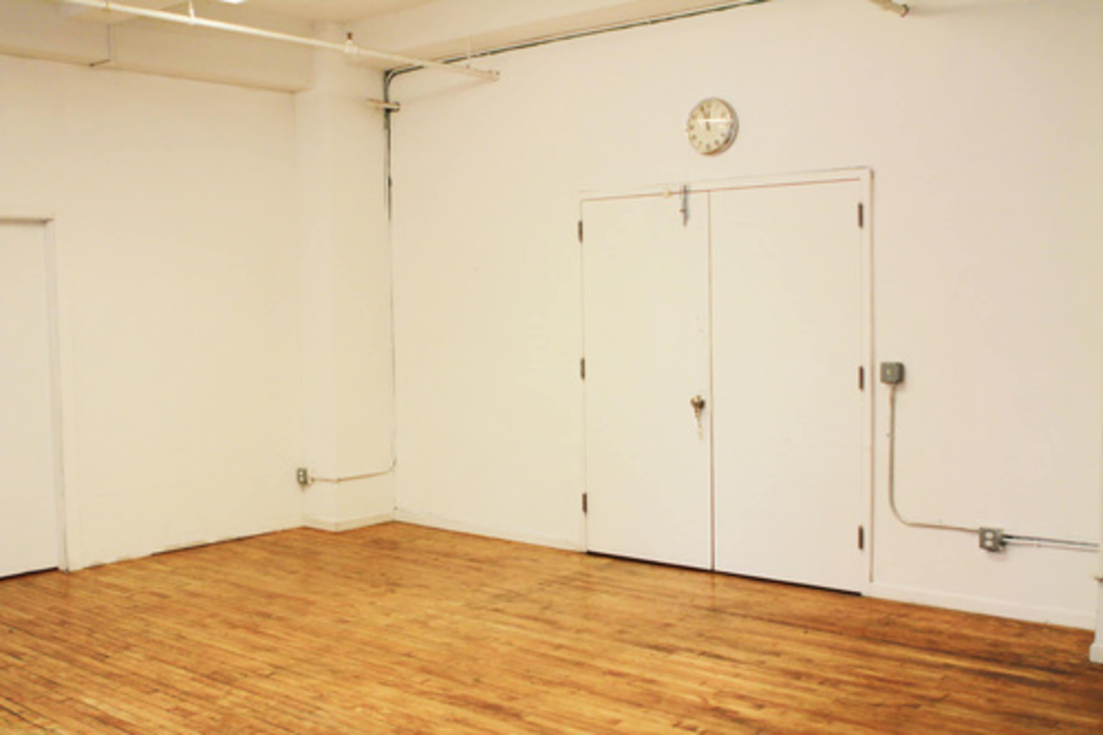 A bare room with wooden floors, white walls, and a clock mounted above a set of double doors.