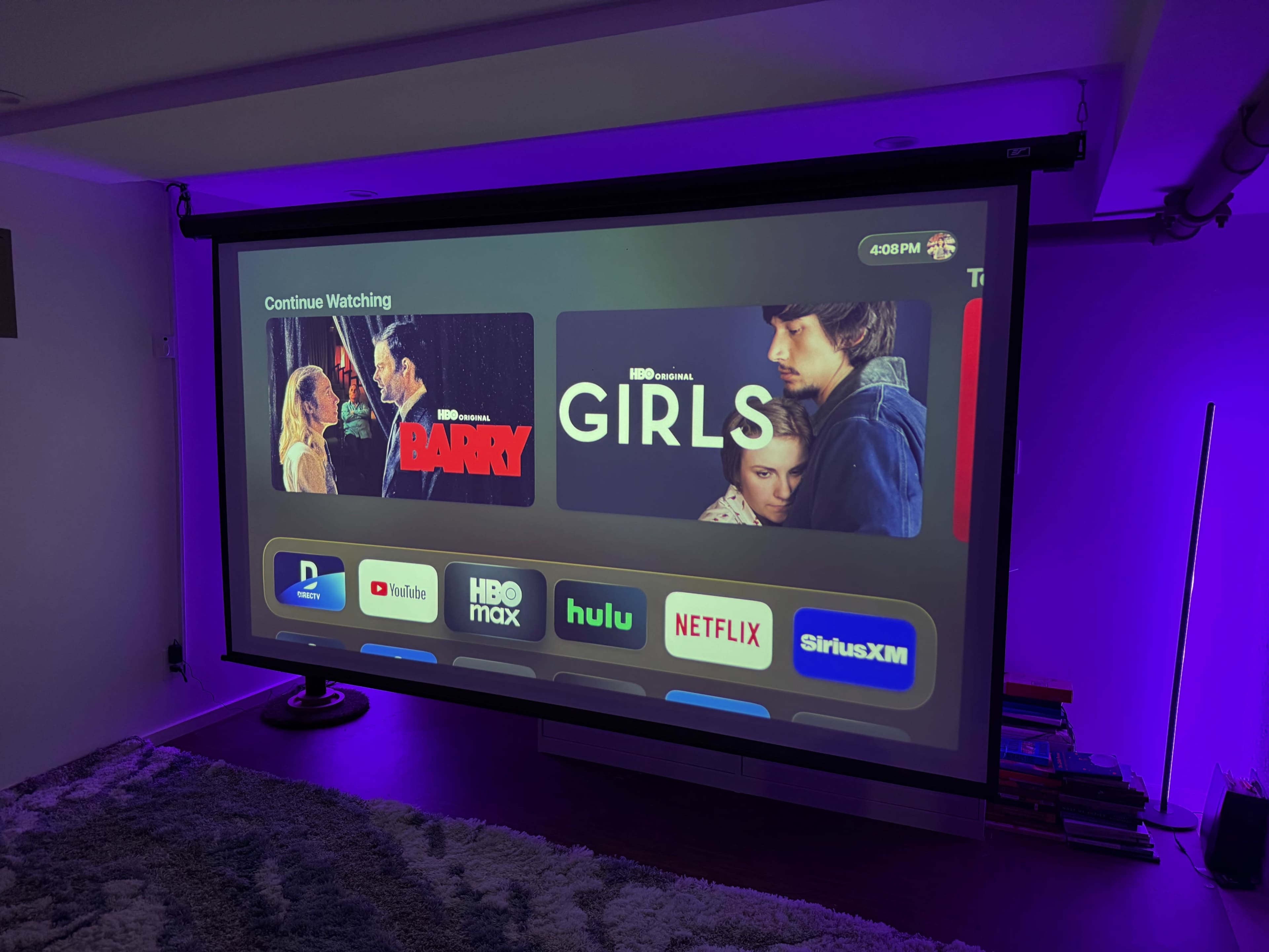 The image shows a projector screen displaying a streaming interface with titles "Barry" and "Girls," along with logos of various streaming services like HBO Max, Hulu, and Netflix.