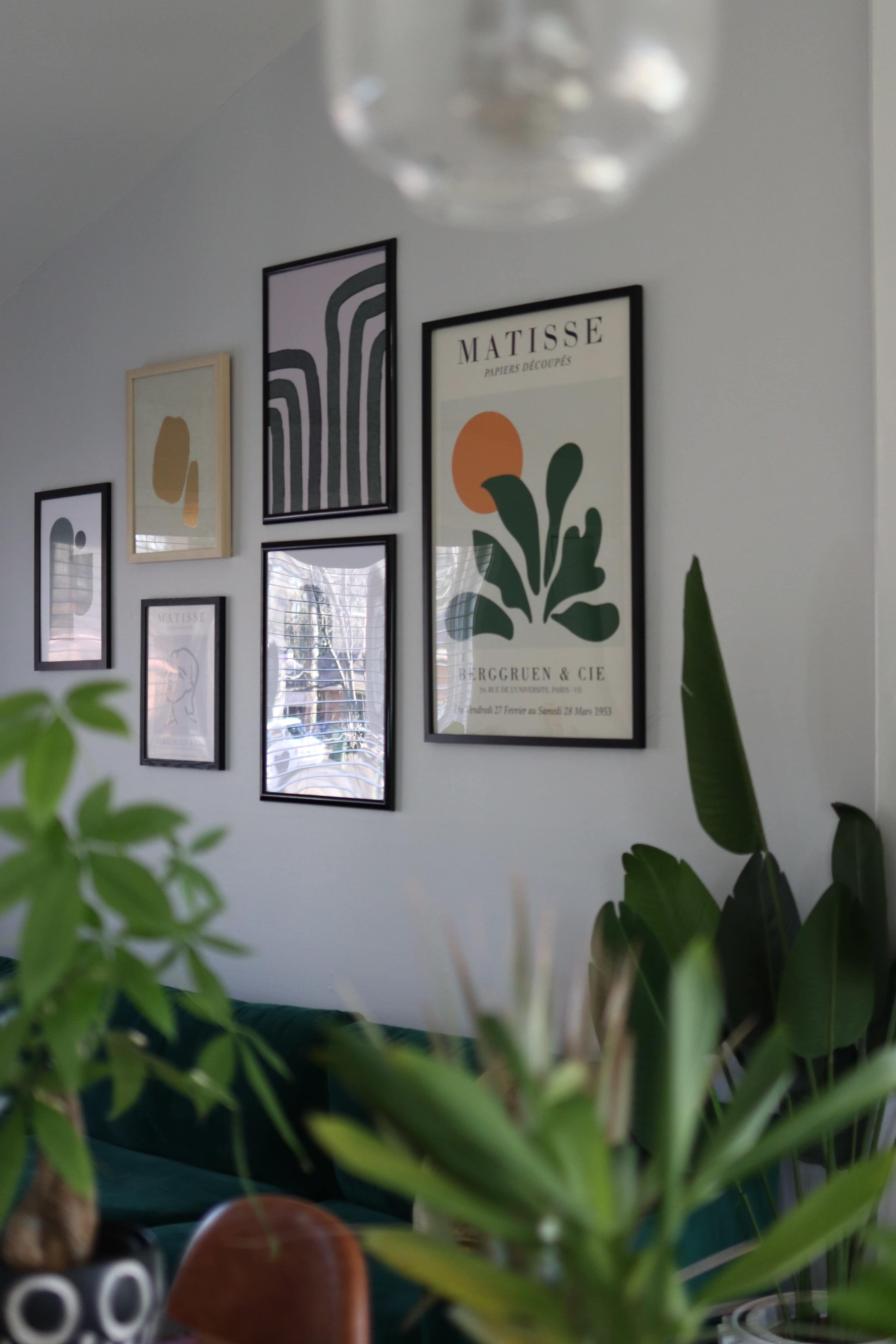 The image features a modern living room with framed art on a light-colored wall, a green sofa, and potted plants positioned in the foreground.