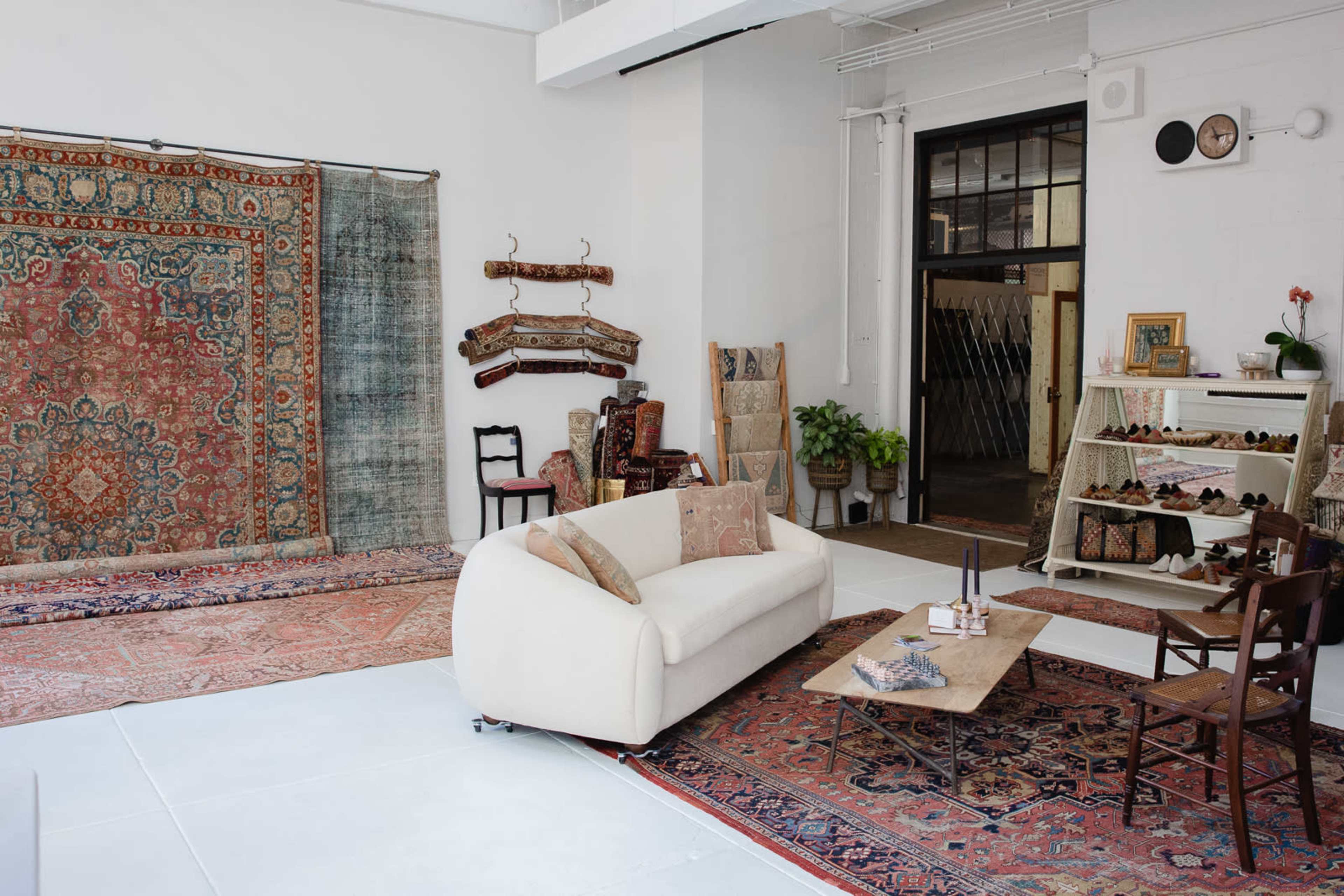 A spacious interior with a white couch, a wooden coffee table, shelves displaying items, and several patterned rugs on the floor.