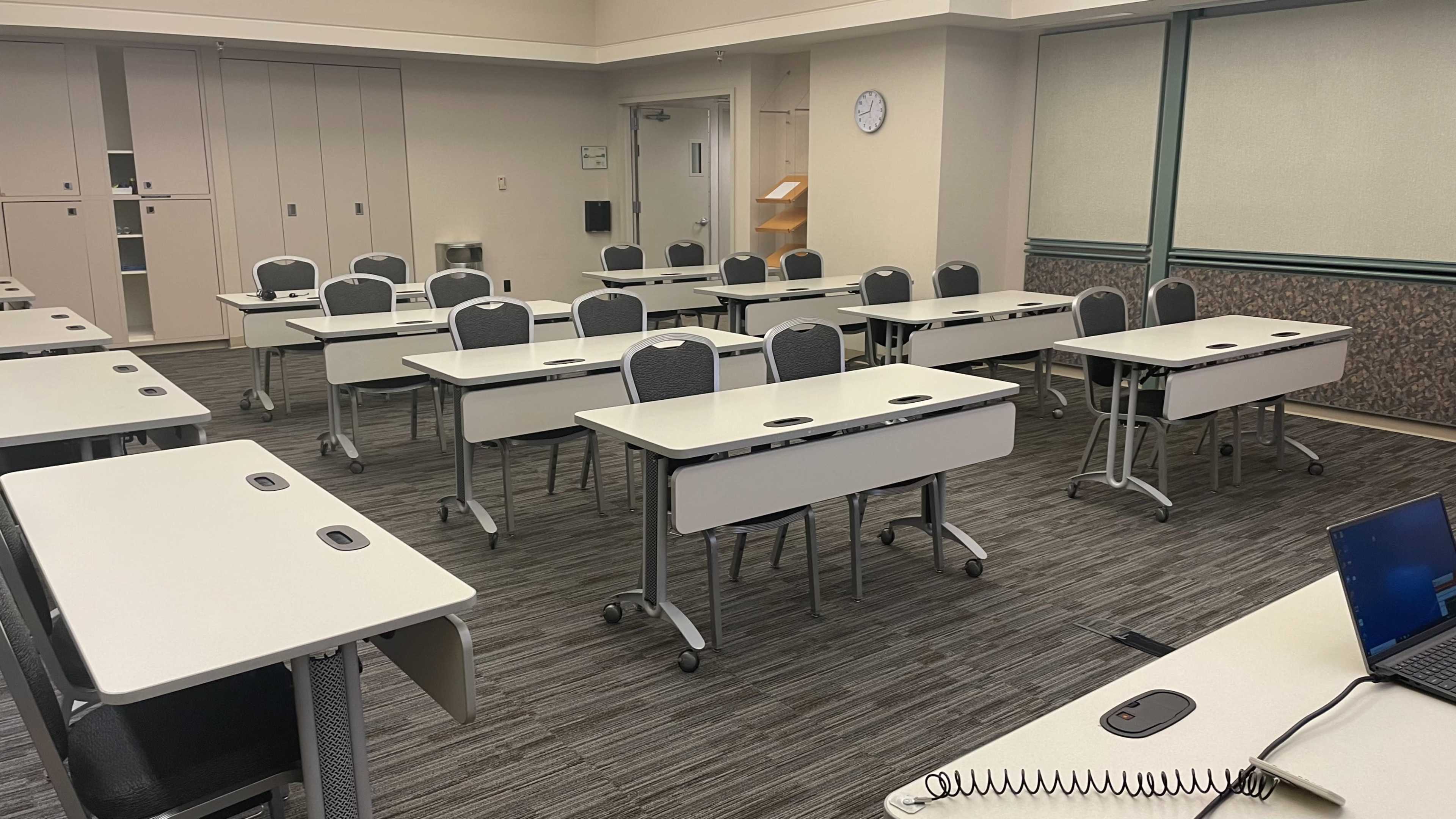 A classroom setup with multiple empty tables and chairs arranged in rows.