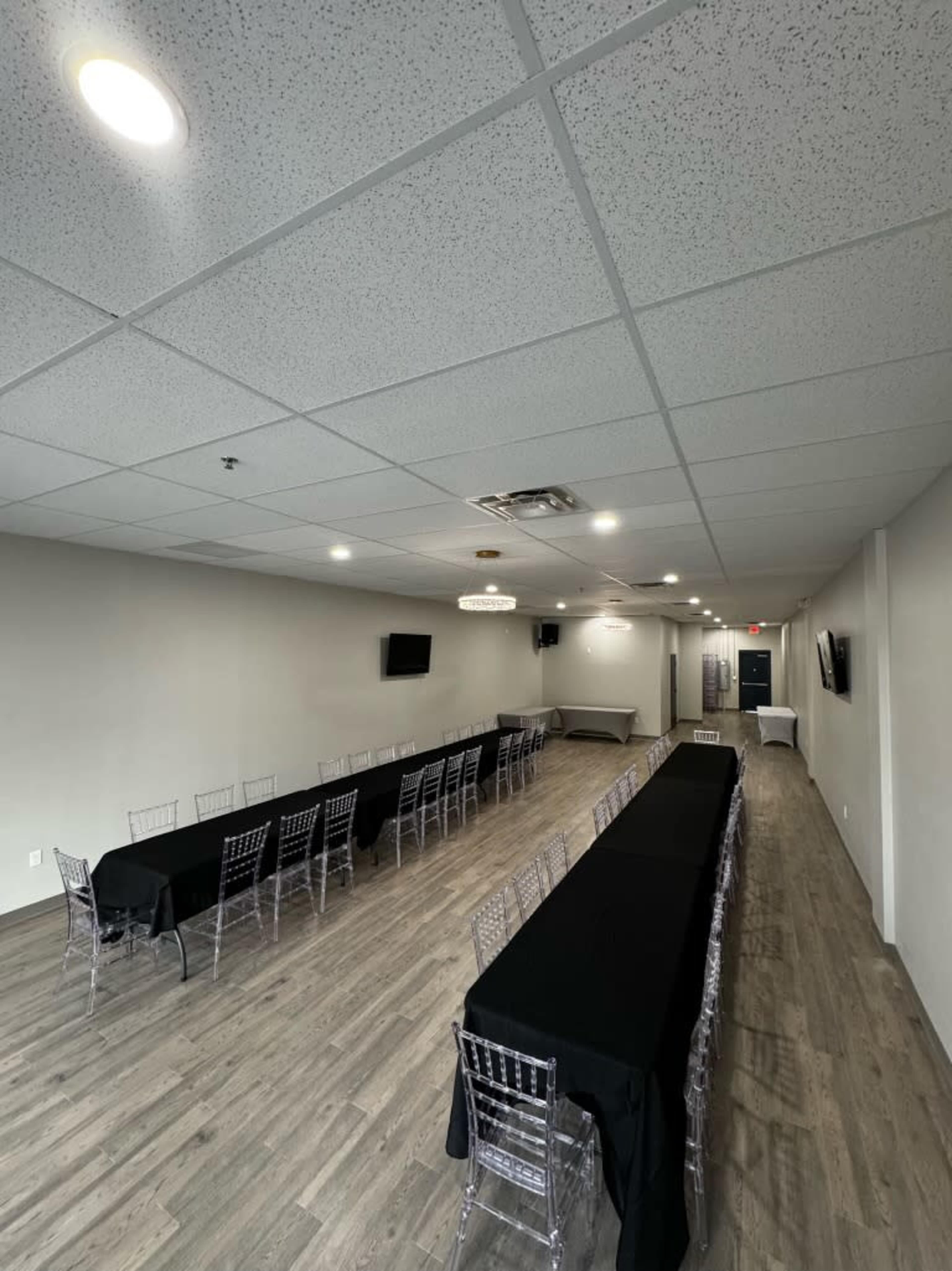 A modern event space features long tables with black tablecloths set up in a well-lit room with a wooden floor and minimal decor.