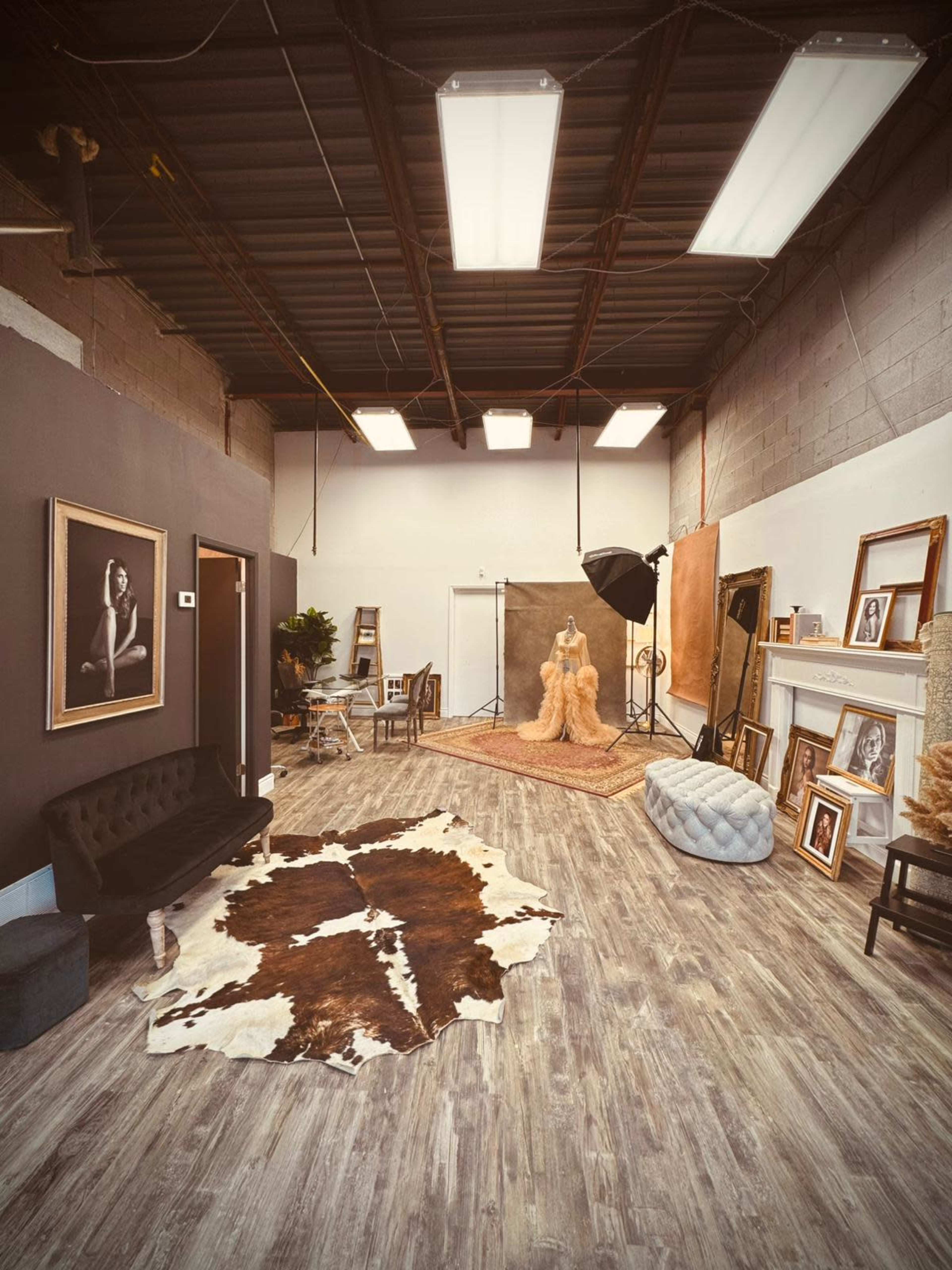 The image shows a photography studio featuring a model, various backdrops, lighting equipment, and several framed portraits displayed on the walls.