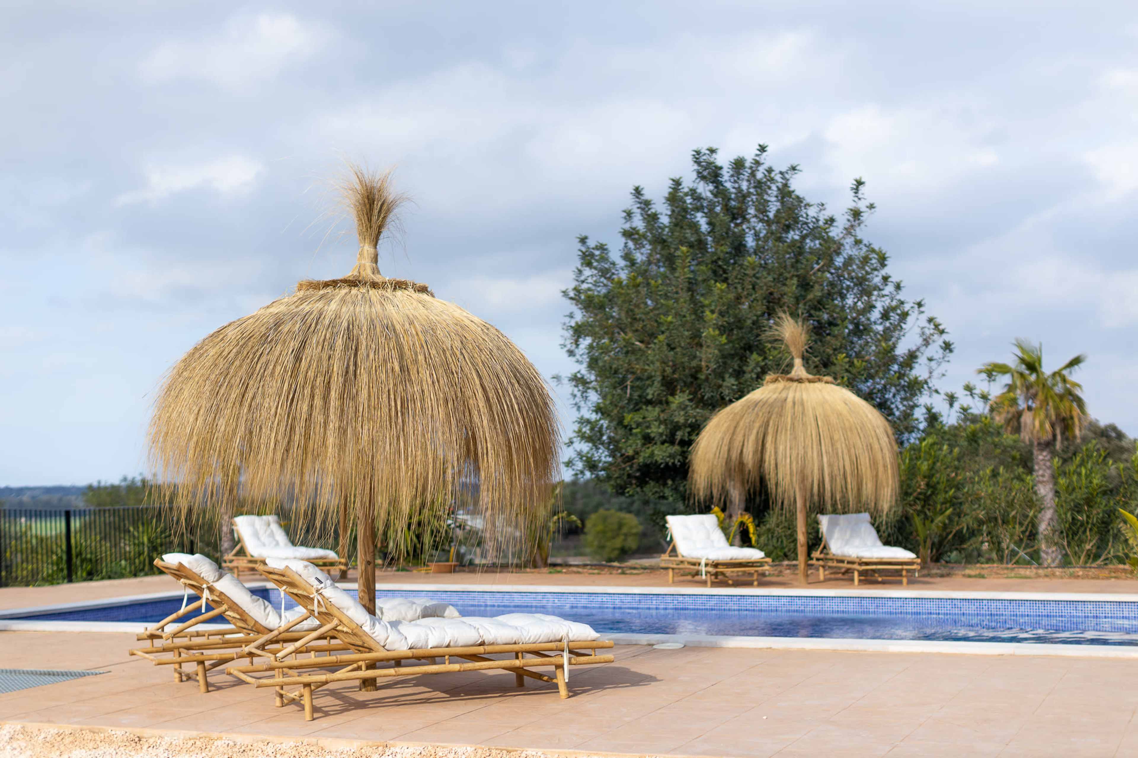 The image shows a swimming pool area featuring two thatched umbrellas and several lounge chairs arranged around the pool.