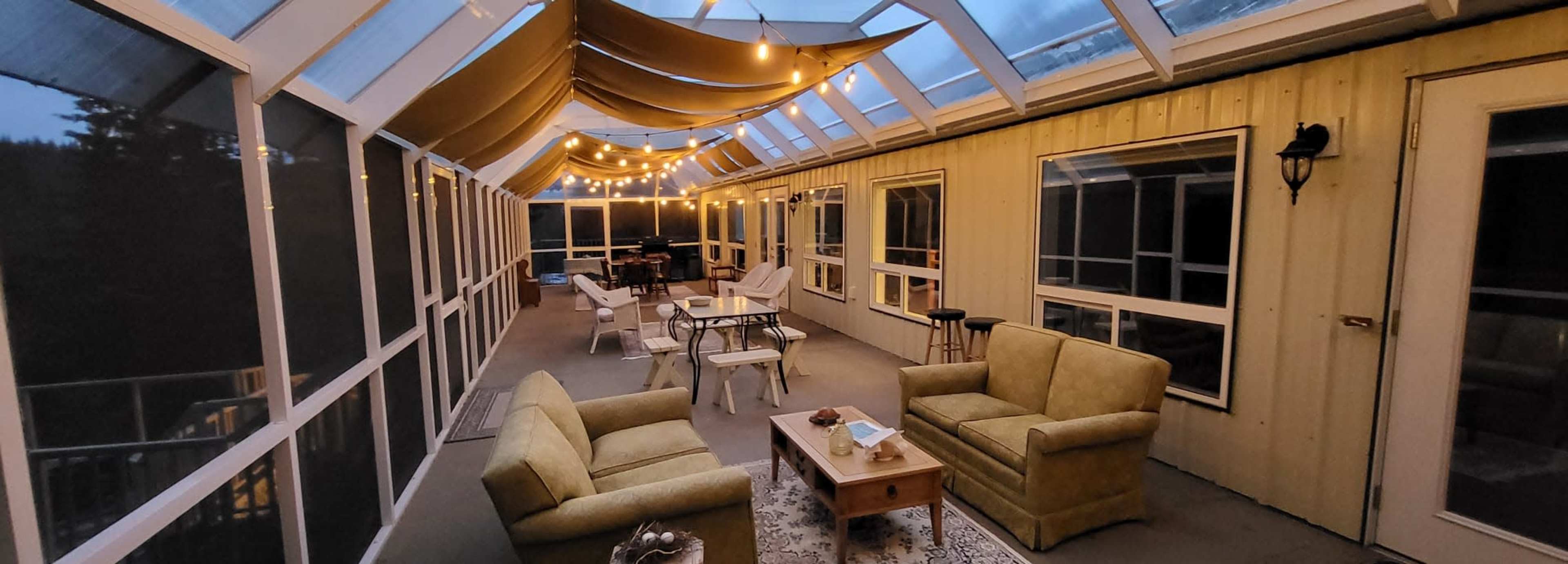A screened-in porch with seating, tables, and string lights overhead.