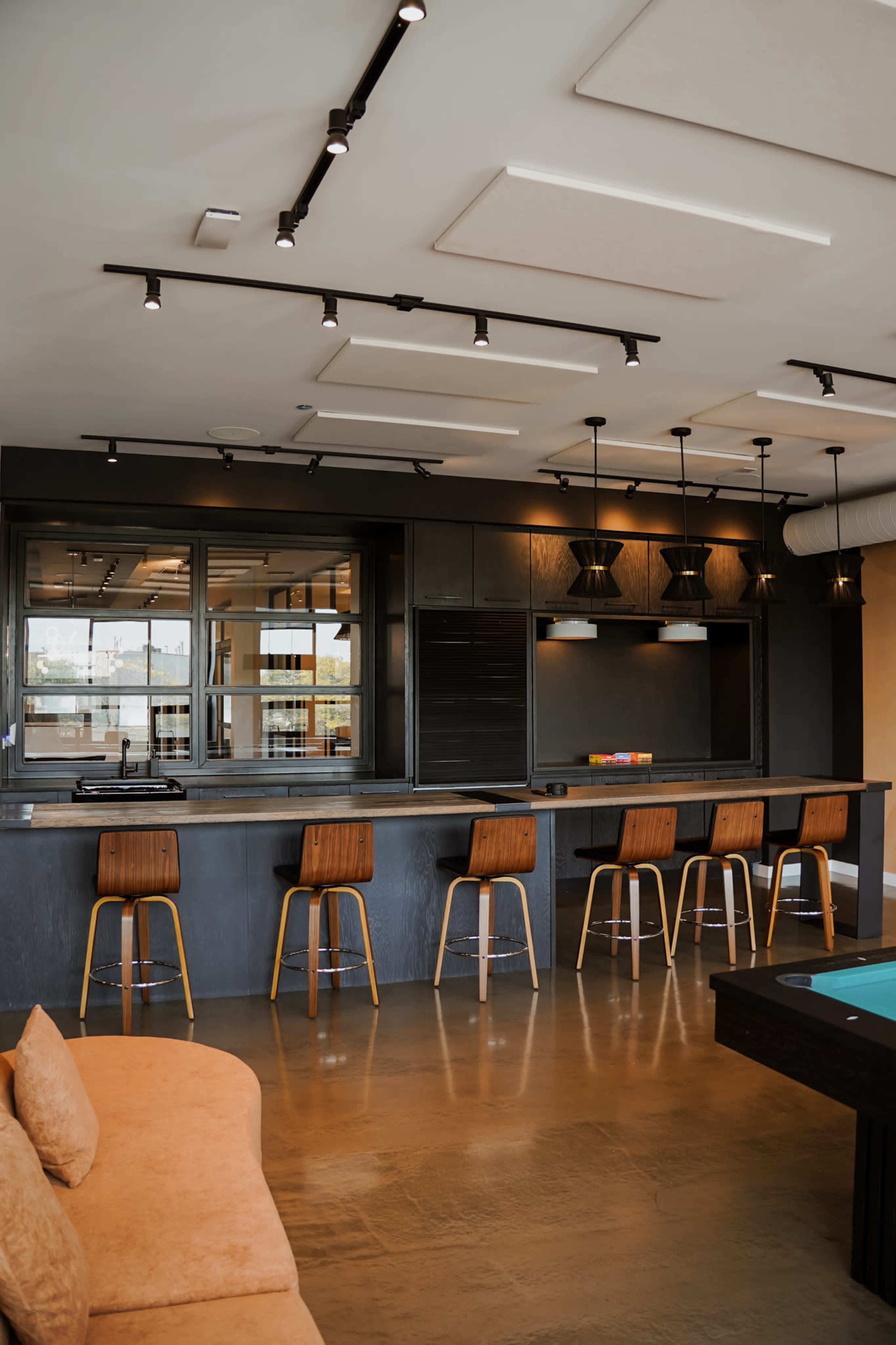 The image shows a modern kitchen and bar area with wooden stools, sleek cabinetry, and pendant lighting.