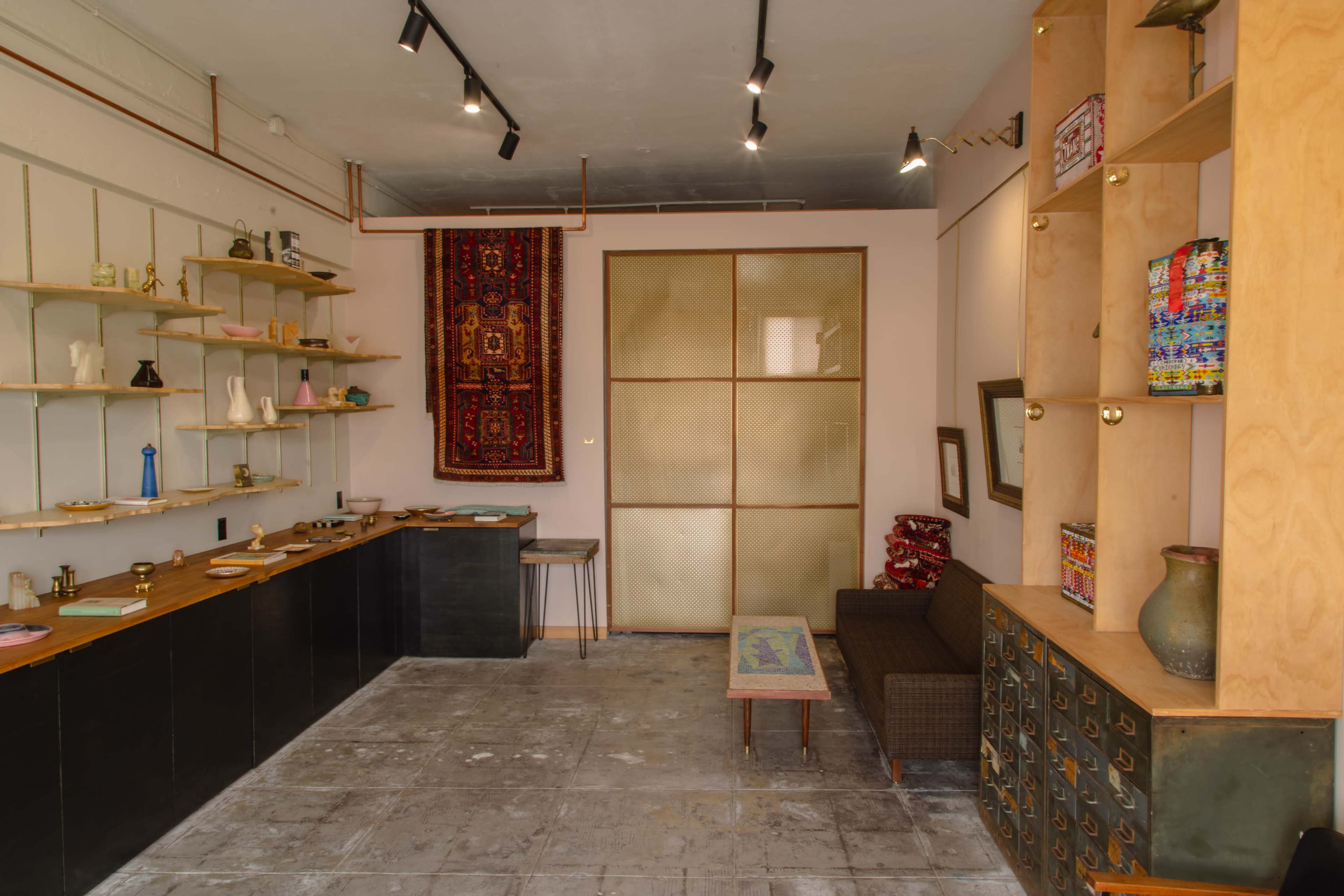 A minimalistic interior of a room with a display shelf on the left, a seating area on the right, and decorative items on various surfaces.