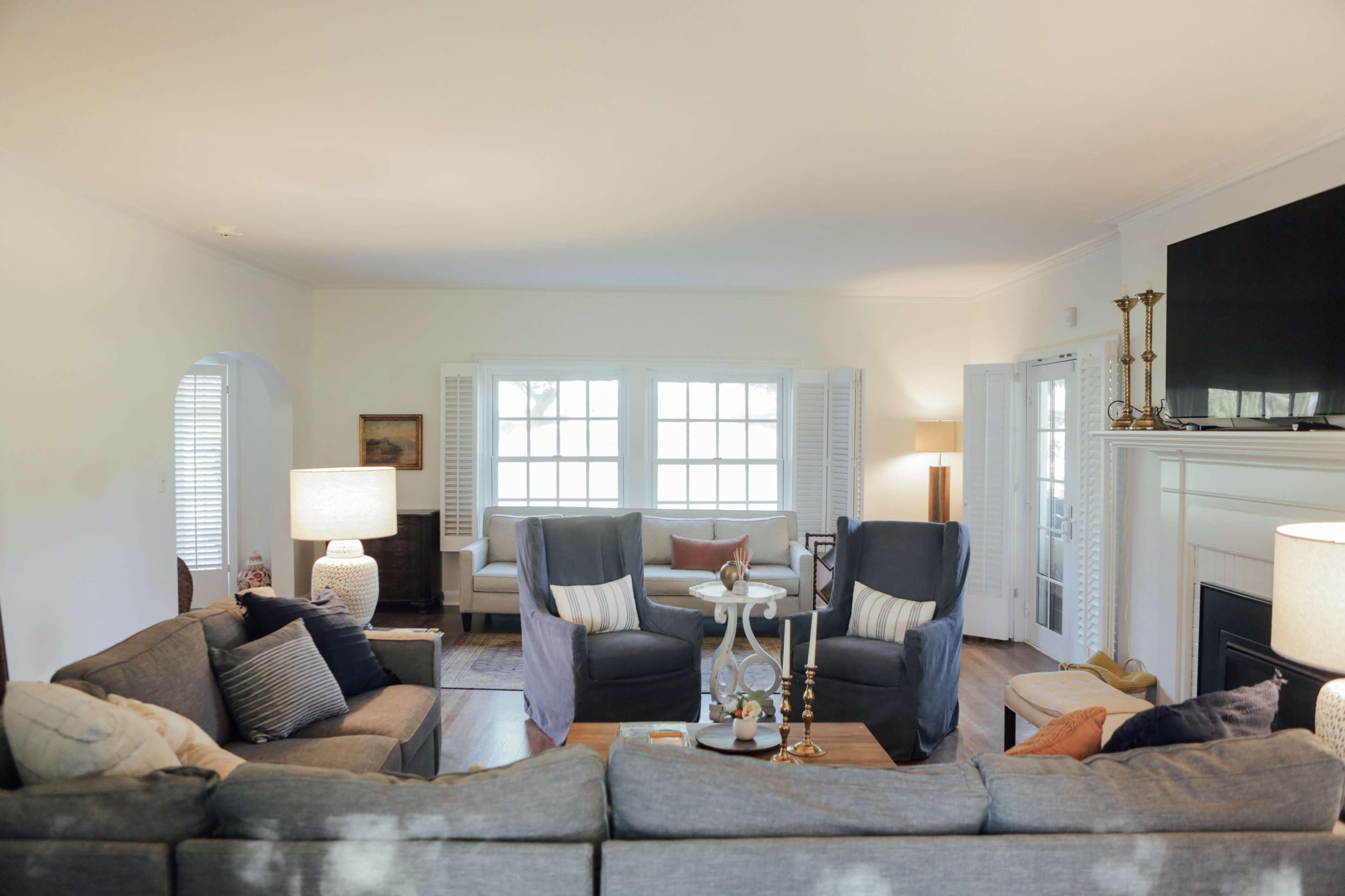 A spacious living room features a sectional sofa, two armchairs, and a coffee table, with large windows allowing natural light to fill the space.