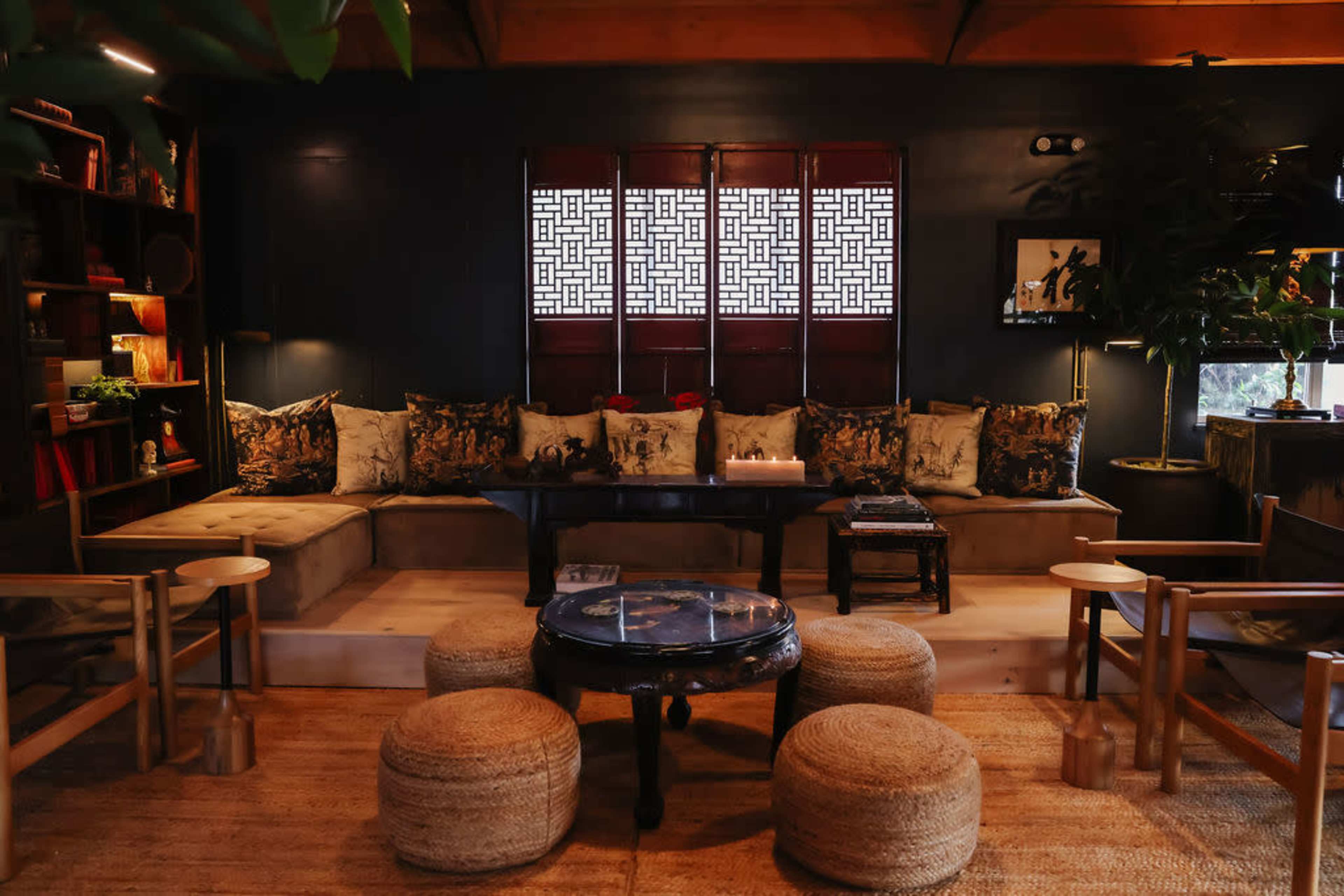 A cozy sitting area with a large cushioned bench, wooden chairs, a circular coffee table, and decorative elements in a warmly lit room.