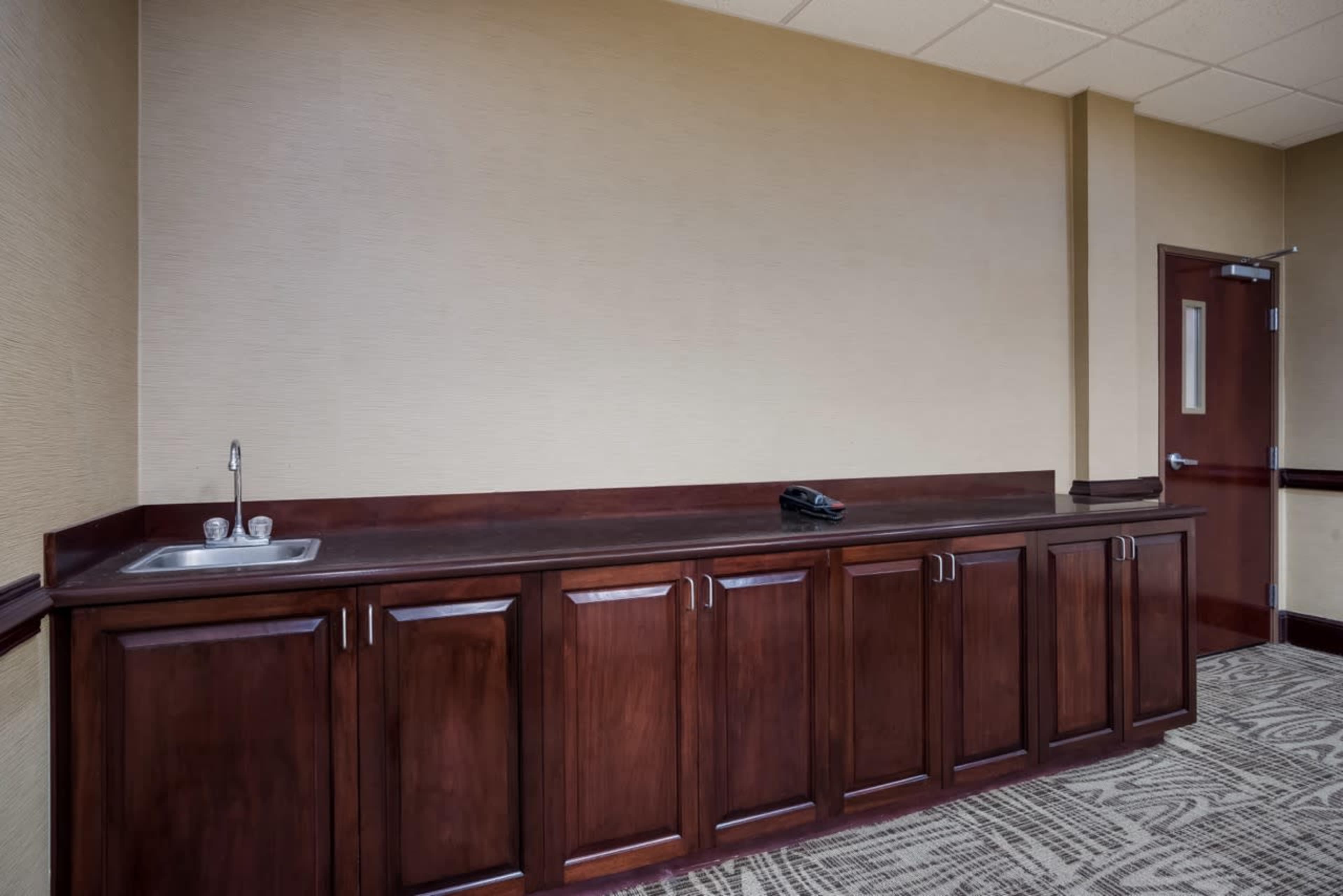 The image shows a simple room with a wooden counter featuring cabinets and a sink, alongside a telephone on top.