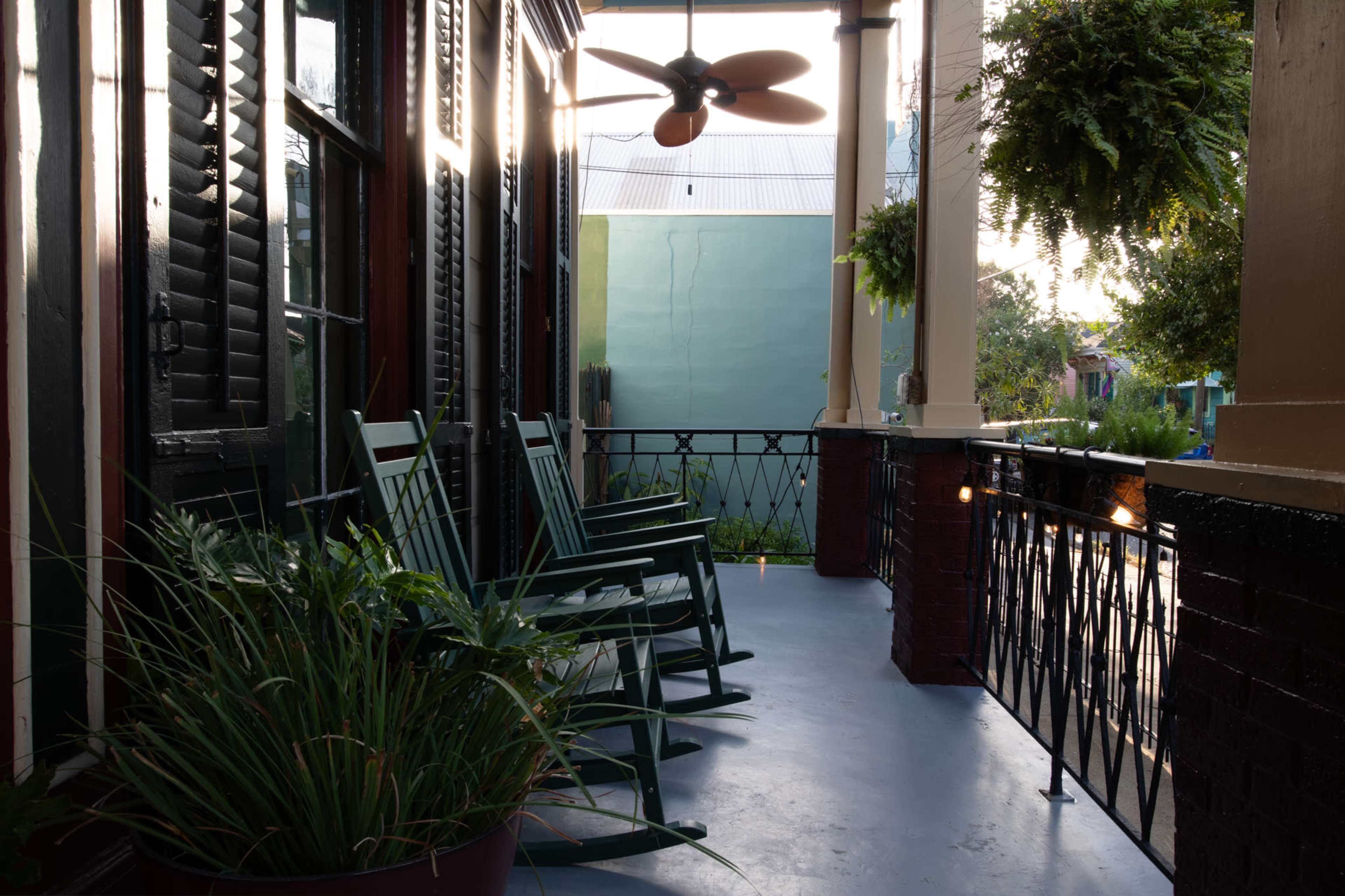 The image shows a porch with green rocking chairs, potted plants, and a ceiling fan, bathed in soft natural light.