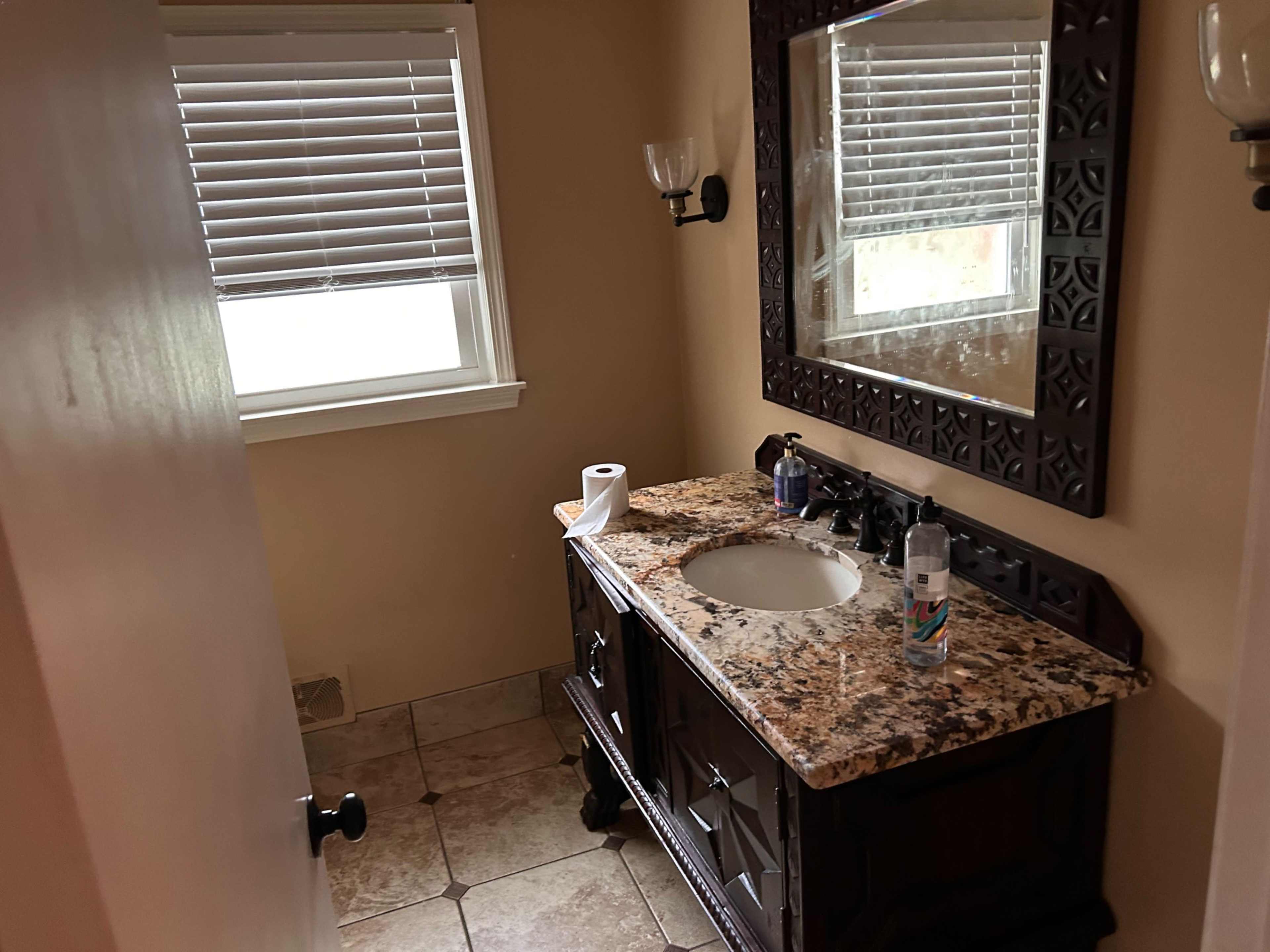 A bathroom features a wooden vanity with a granite countertop, a sink, and a mirror above it, flanked by wall sconces.
