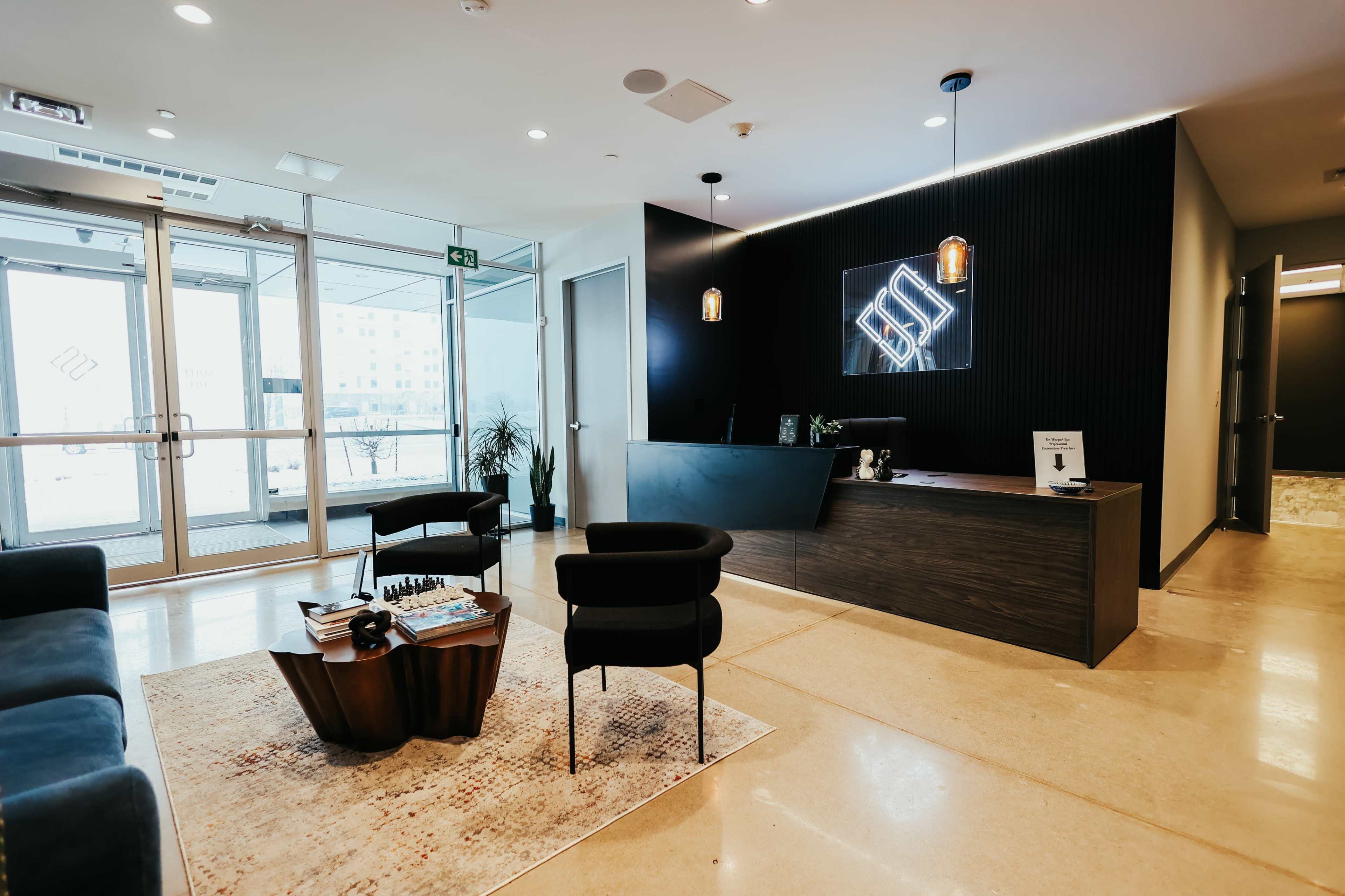 A modern reception area with a dark wood front desk, seating arrangements, and large glass doors leading to an outdoor view.