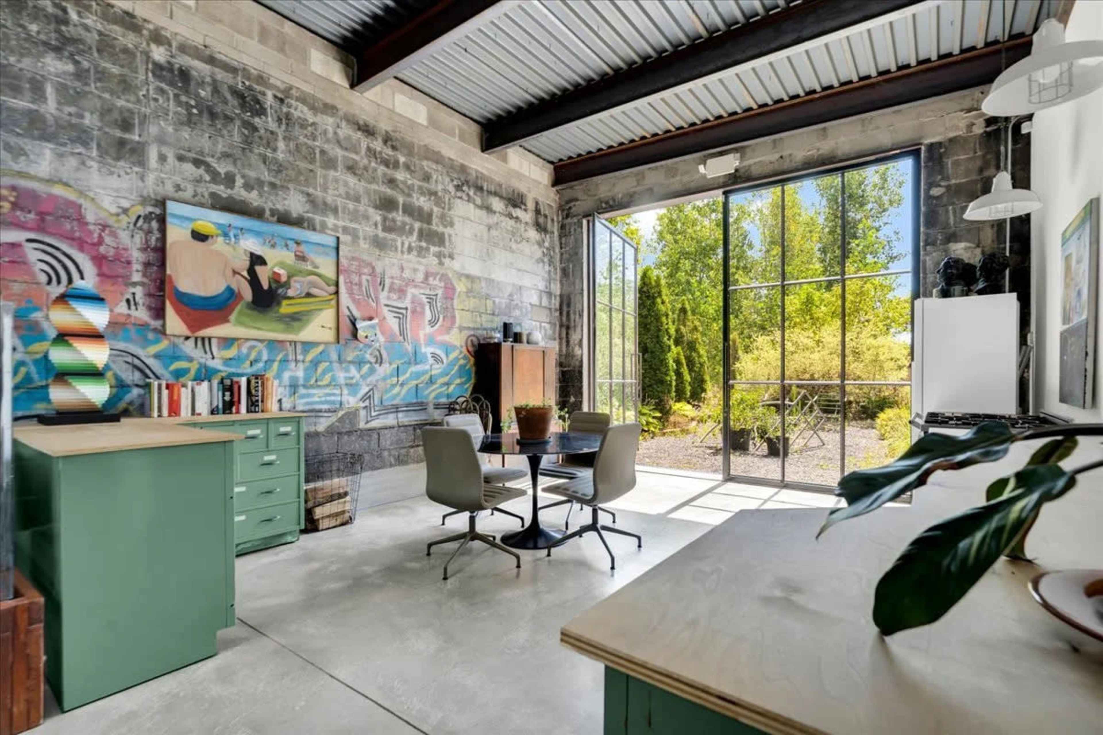 A modern workspace features a blend of industrial concrete walls and large windows, with a table and chairs arranged under natural light.